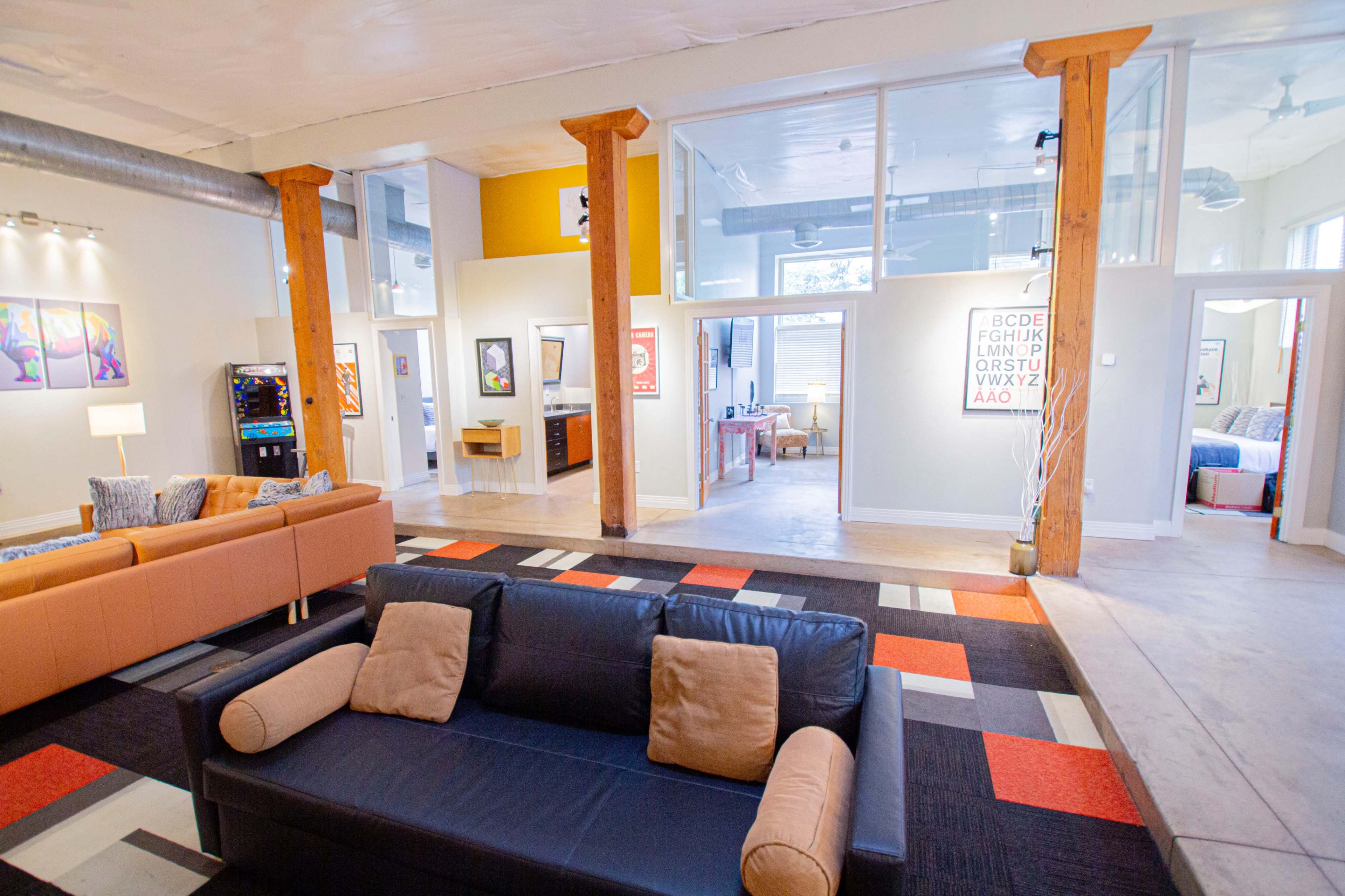 The interior of a modern, open-concept space features a black sofa, colorful area rugs, and various framed artworks on the walls.