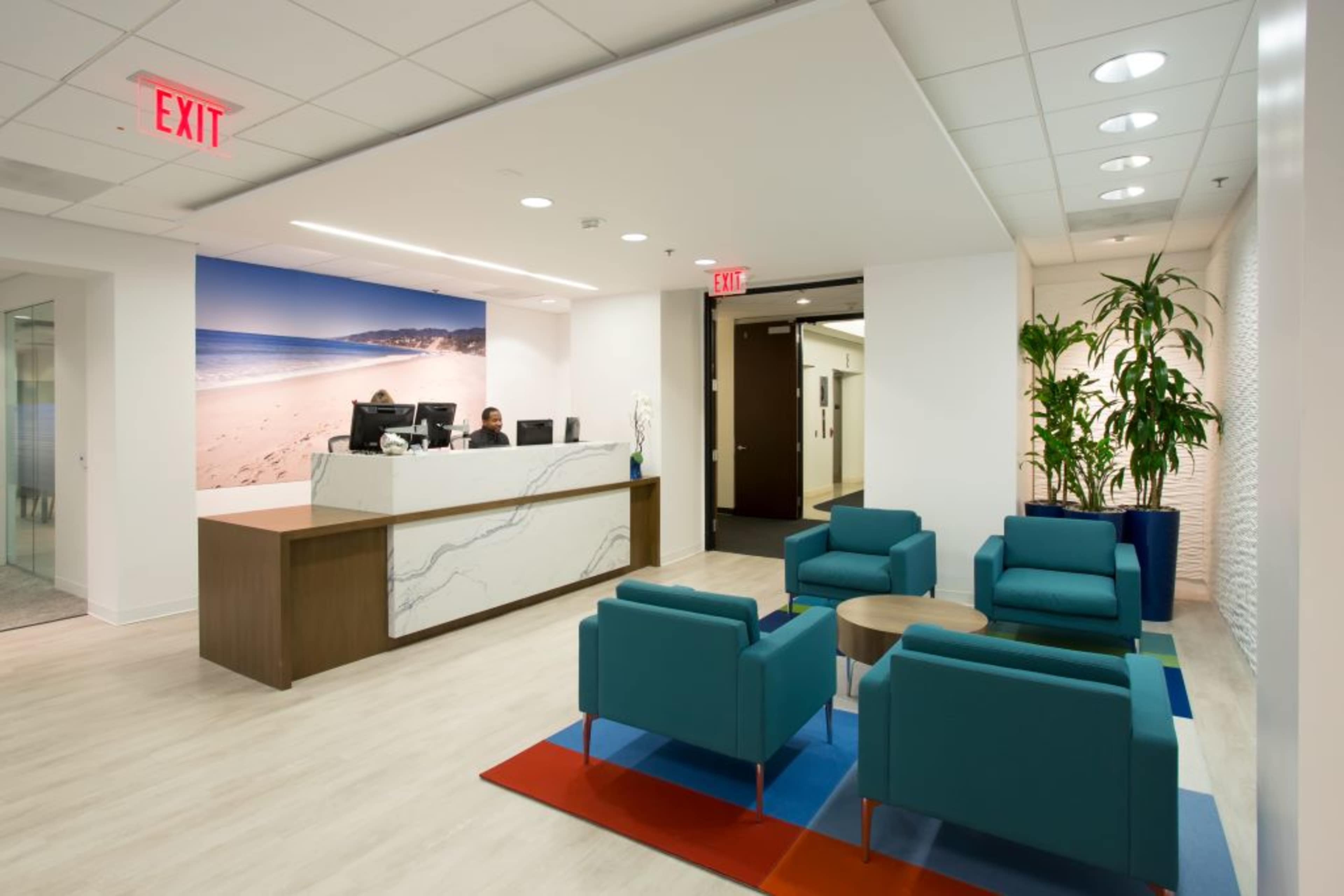 A modern reception area features a marble front desk, green seating arrangements, and a beach-themed mural on the wall.
