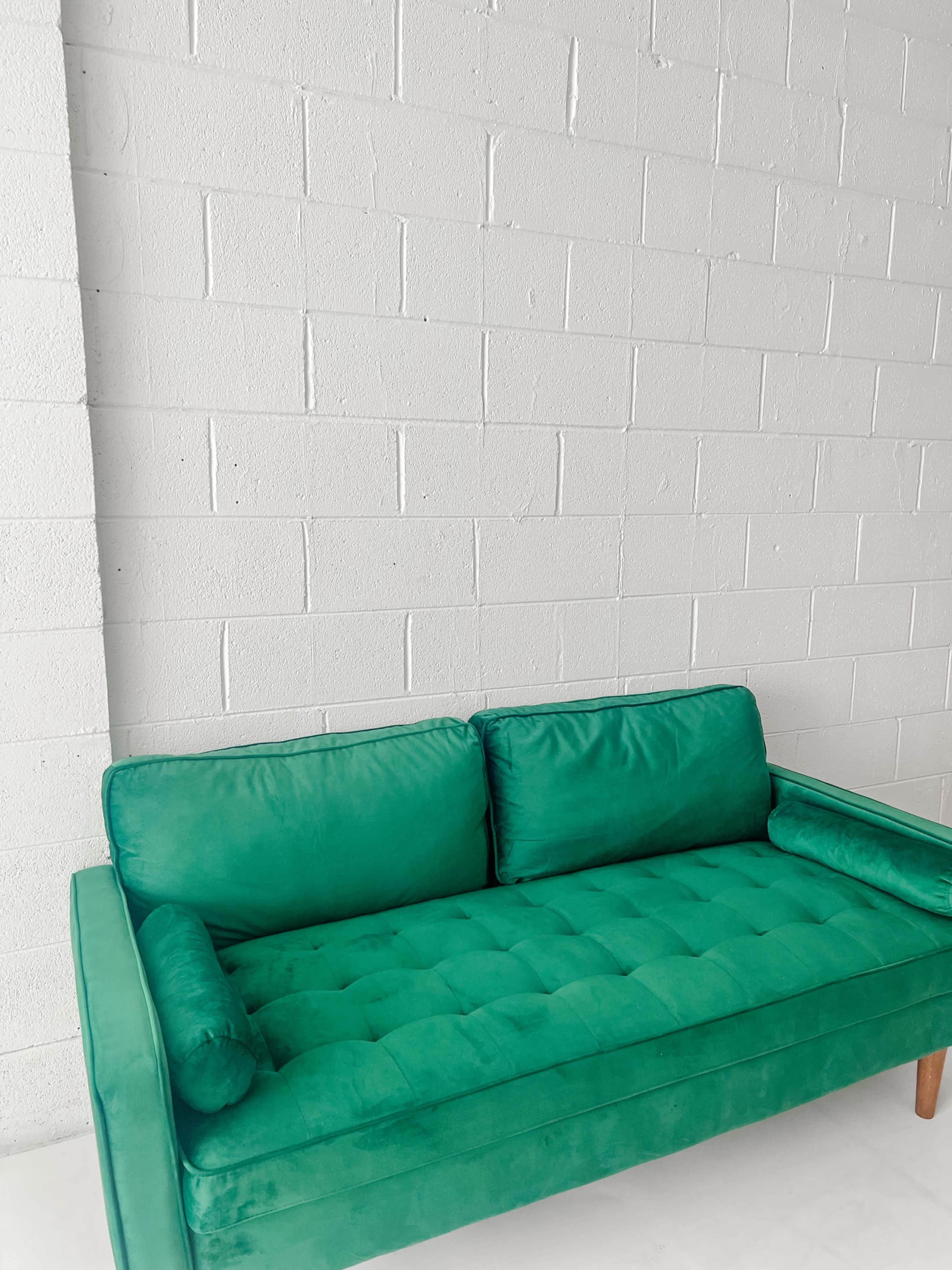 A green velvet couch is positioned against a white block wall.