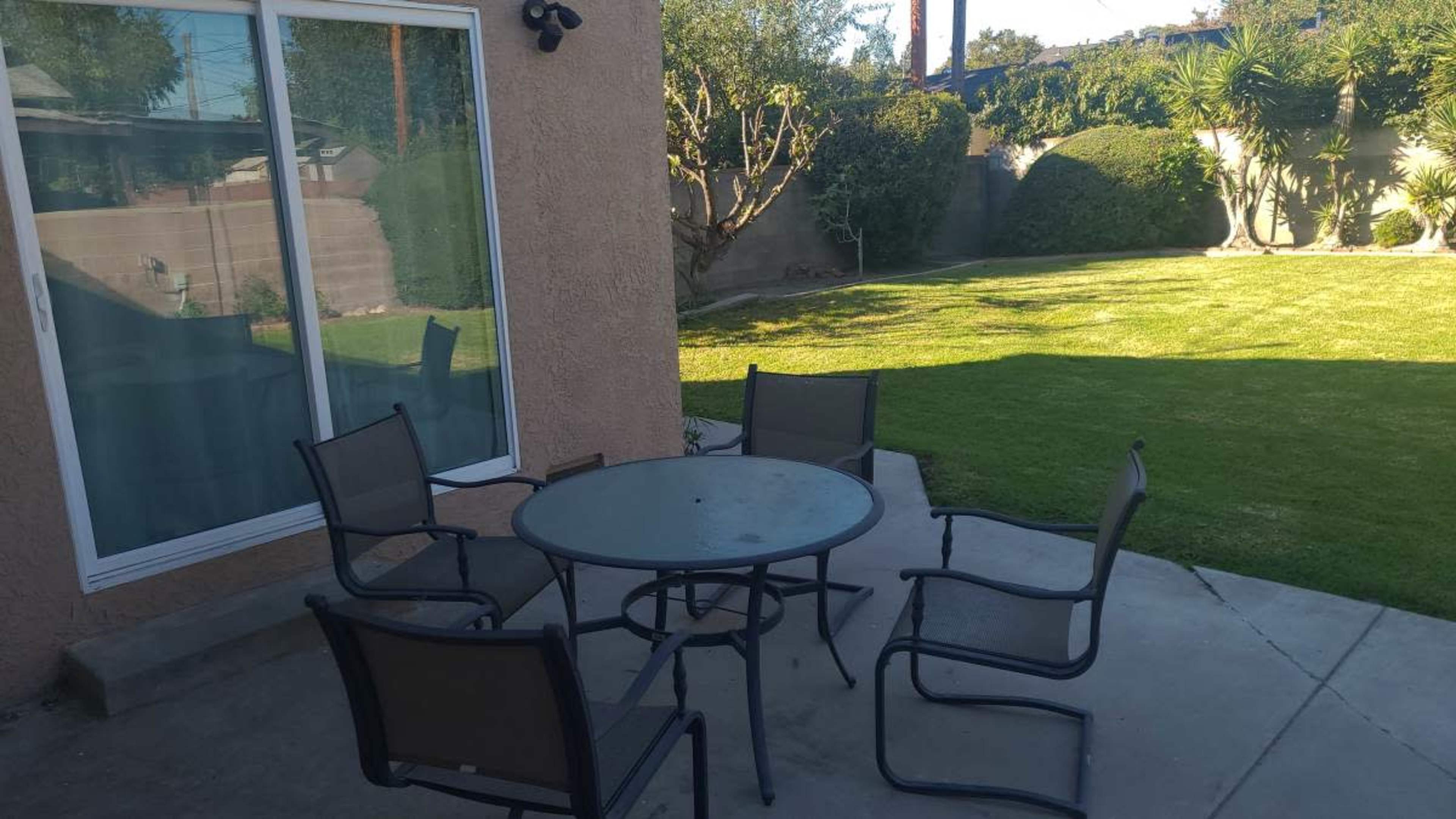 A patio area features a round table surrounded by five chairs, with a grassy backyard visible in the background.