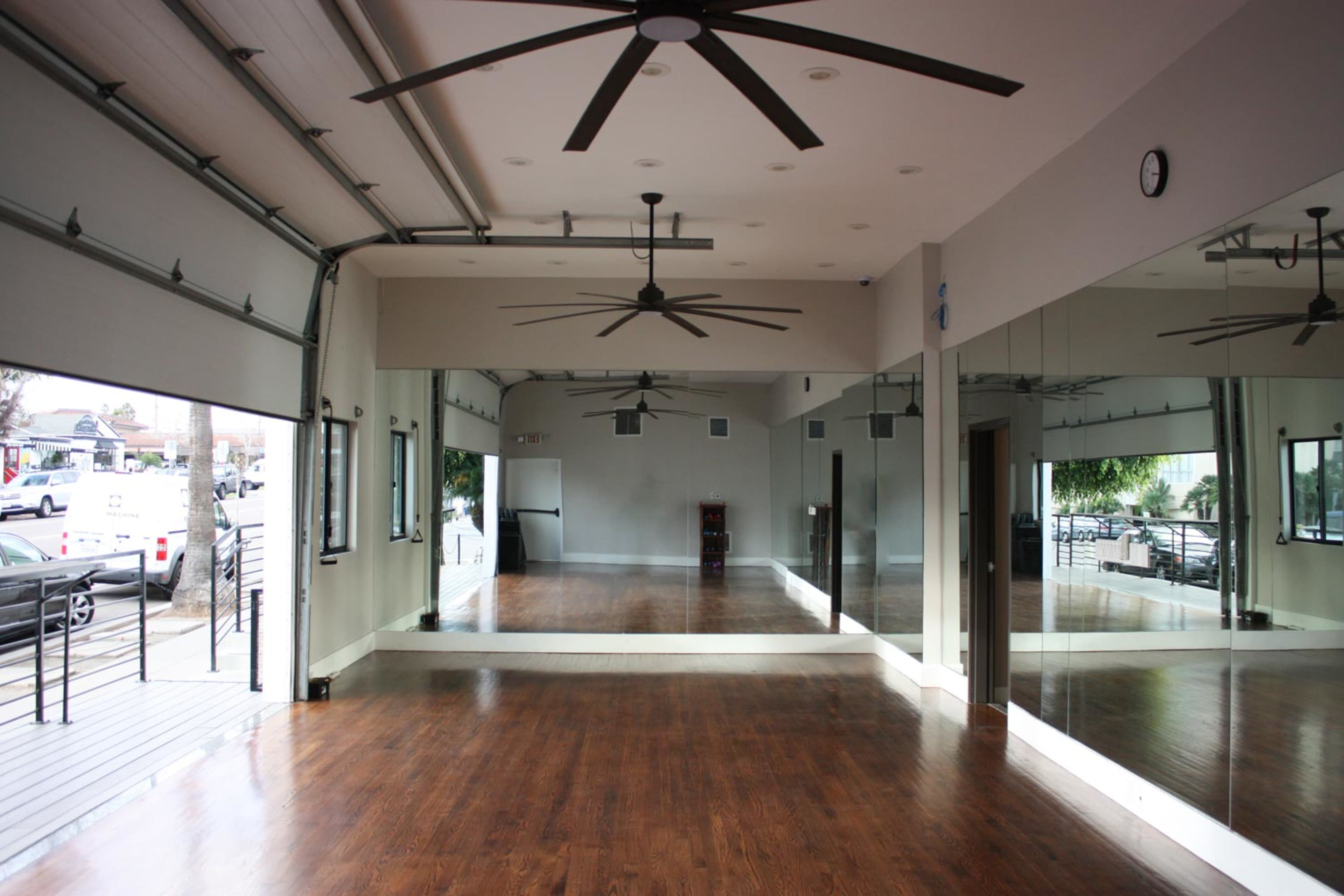 A spacious room with hardwood floors, large mirrors on one wall, and a ceiling featuring multiple overhead fans.
