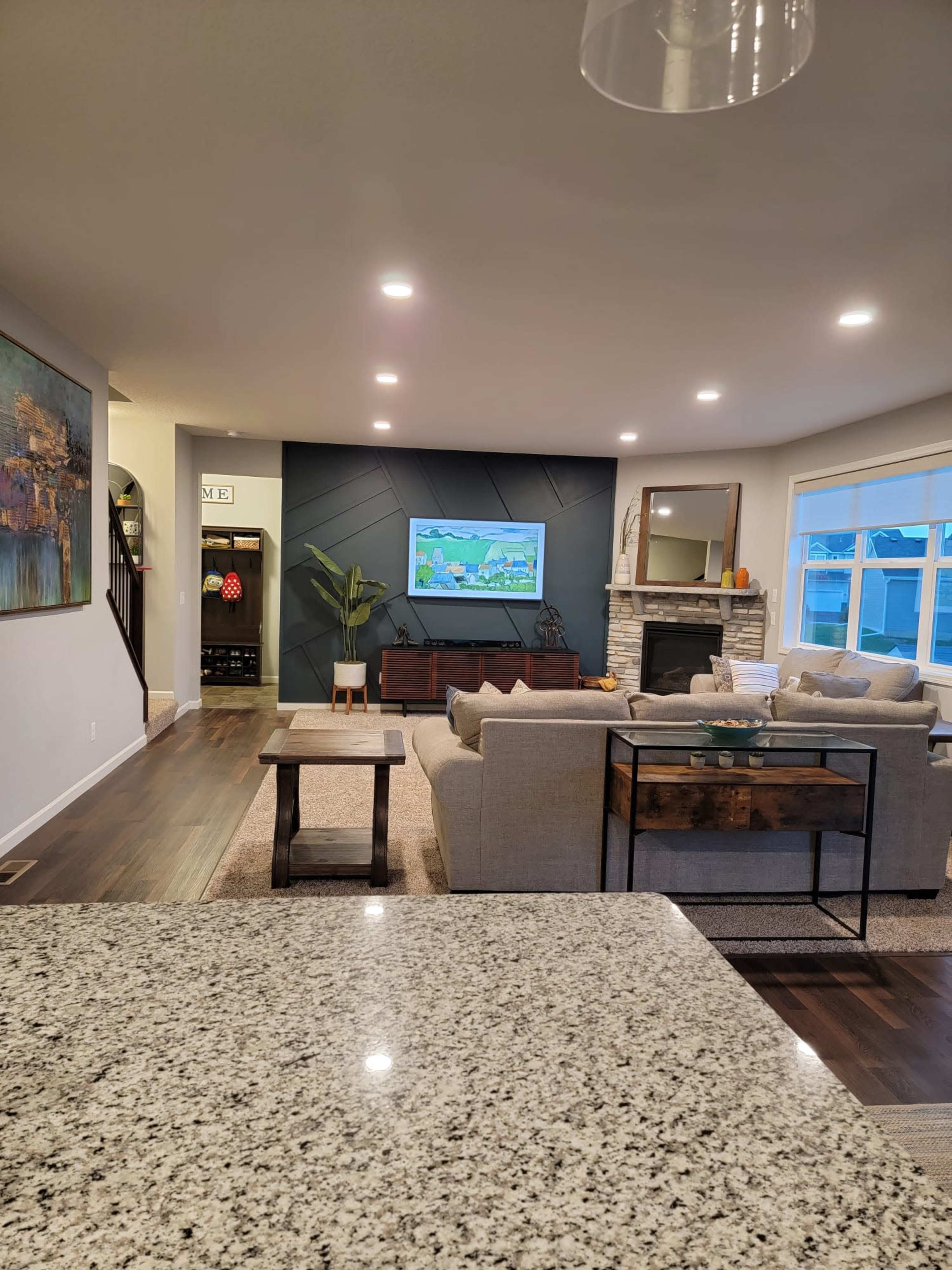 A modern living room features a large sofa, a coffee table, and a television mounted on the wall, with a stone fireplace and decor elements in the background.