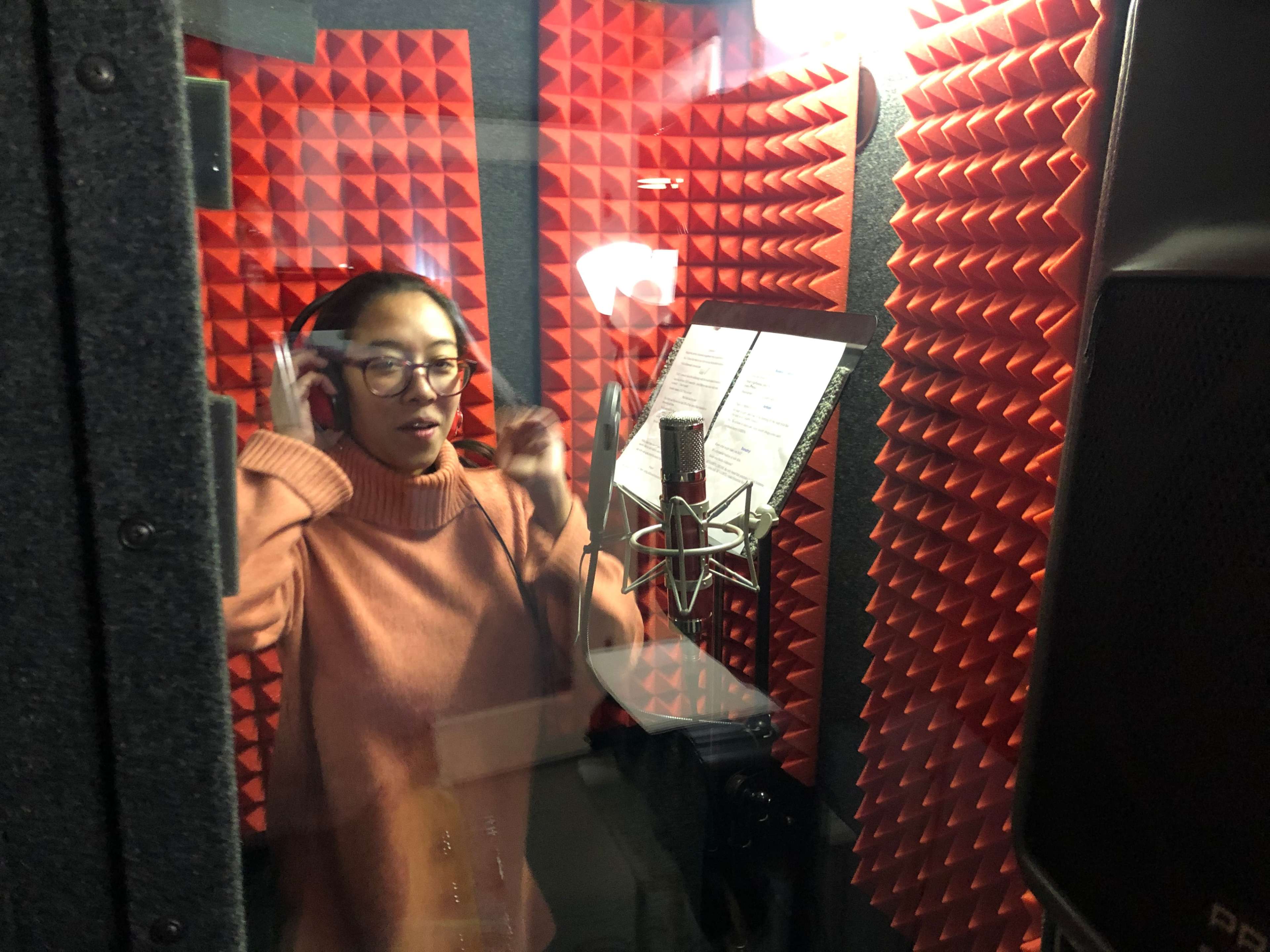 A person wearing headphones is singing in a soundproof recording booth with red acoustic foam walls.