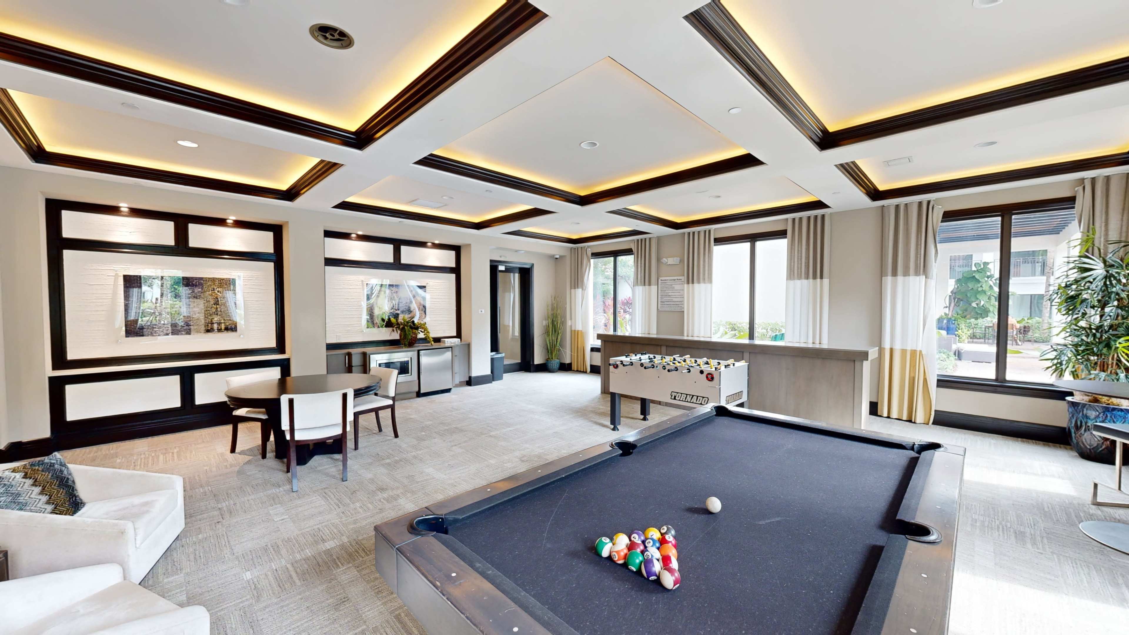 A well-lit recreational room featuring a pool table, foosball table, and modern seating arrangements.