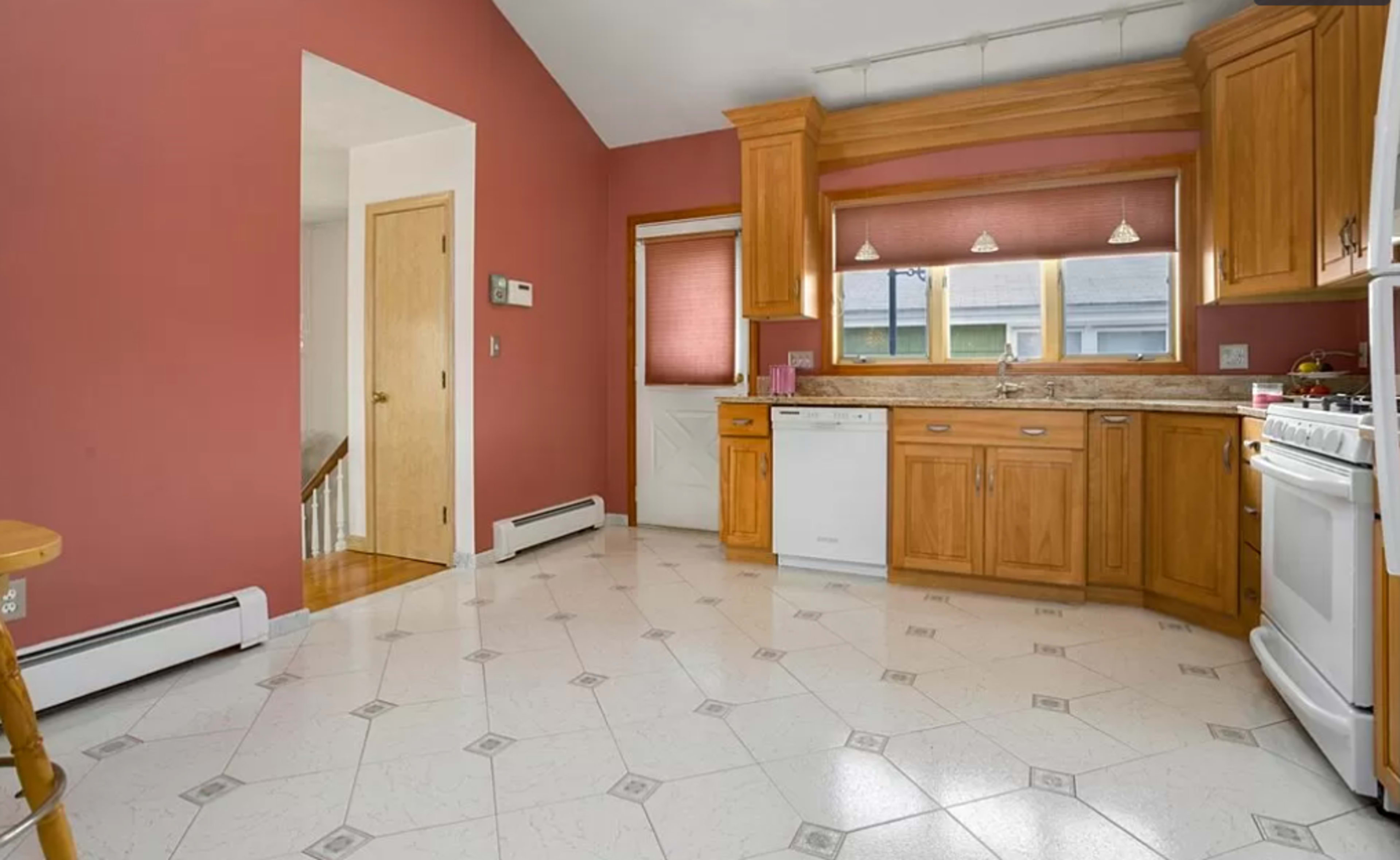 The image shows a kitchen with wooden cabinets, white appliances, and a pink wall.