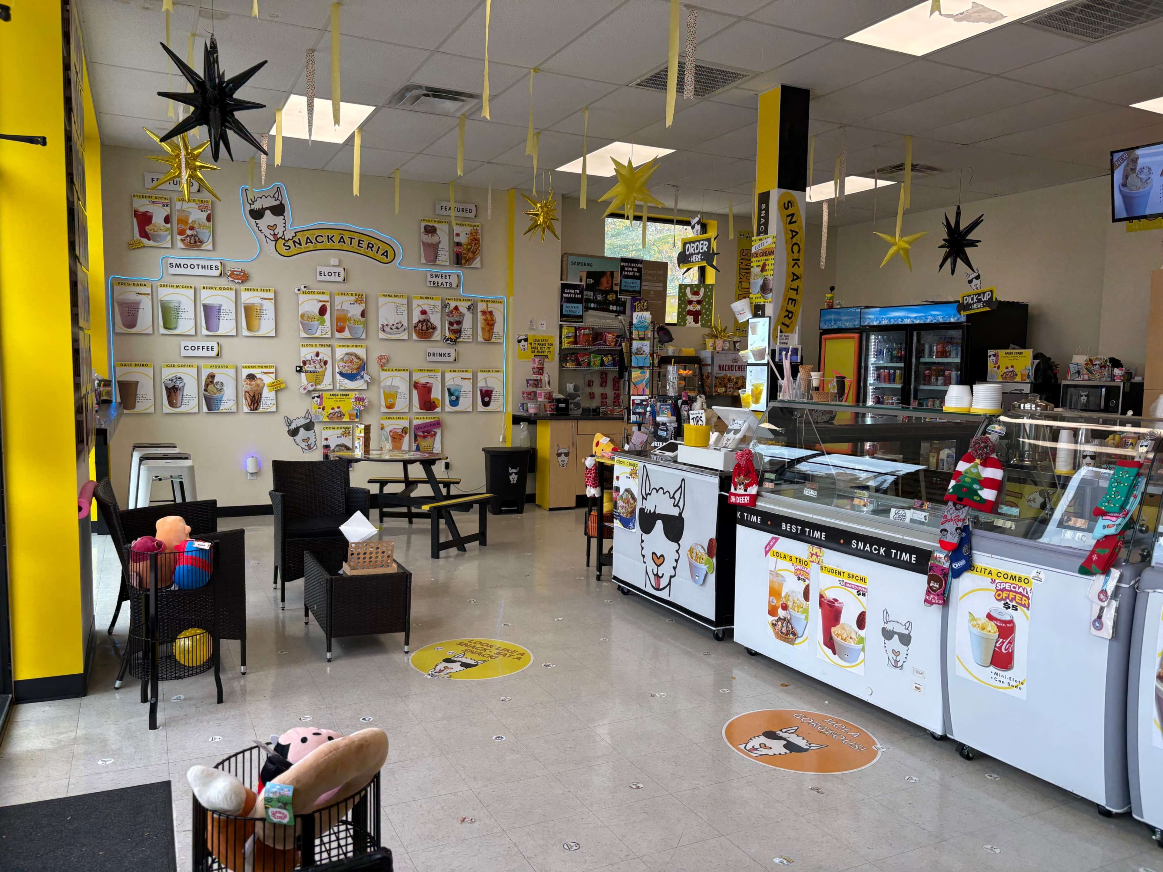 The image shows an ice cream shop interior with a brightly colored yellow and black theme, featuring a service counter, various menu items displayed on the walls, and decorative stars hanging from the ceiling.