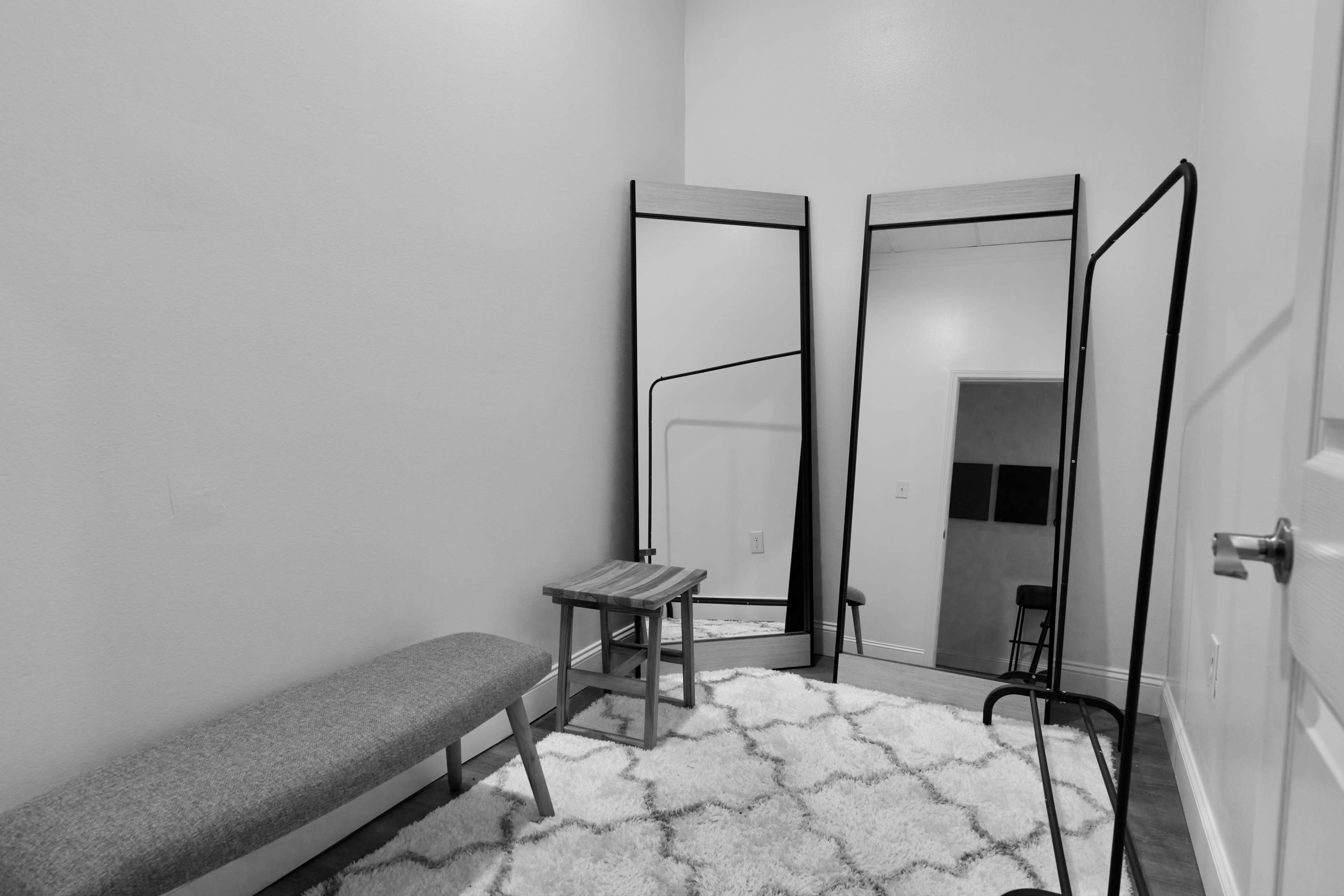 A minimalist room with two large mirrors, a bench, a small wooden table, and a light-colored rug.