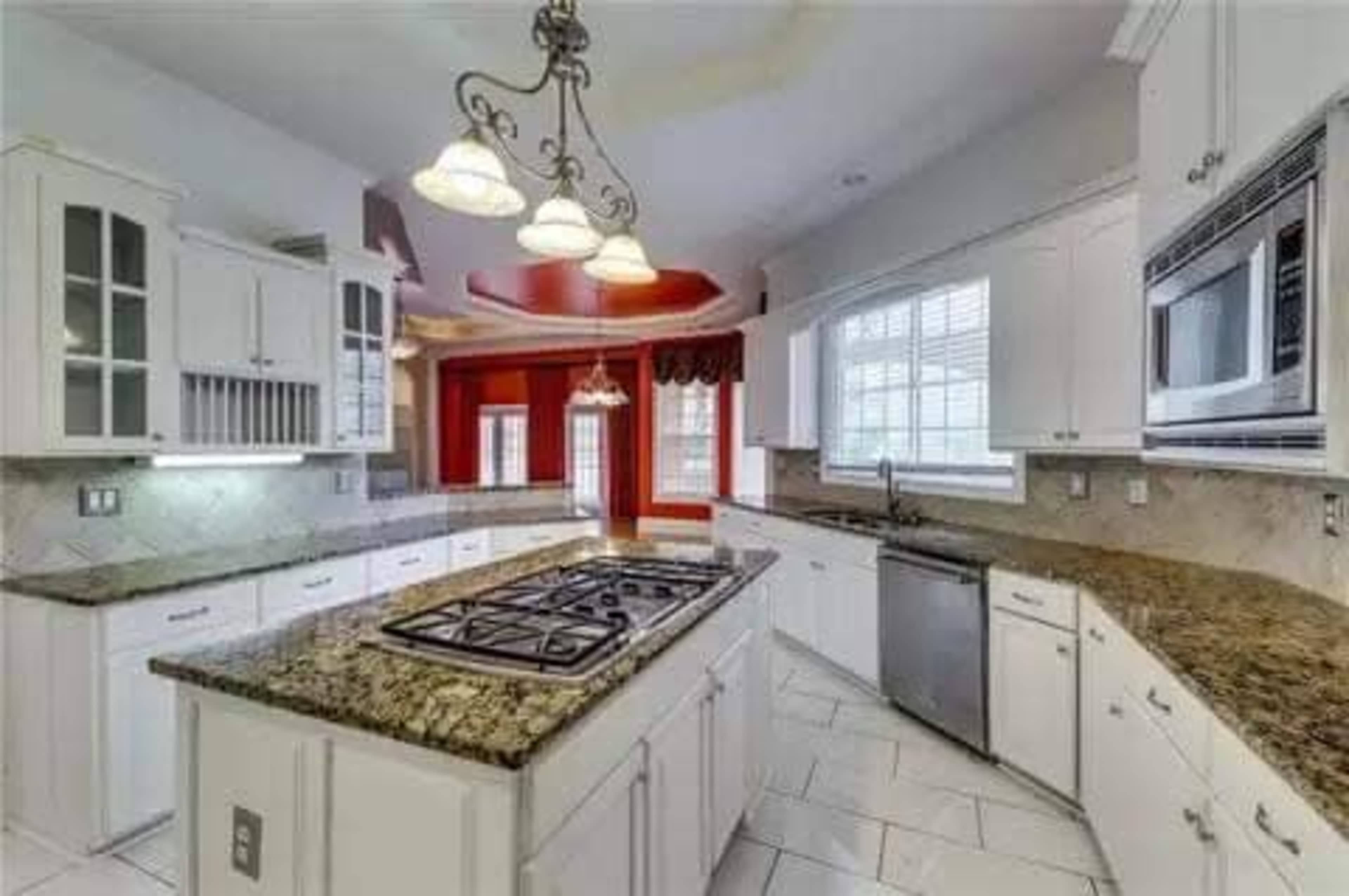 A modern kitchen with white cabinetry, a central island with a gas stove, and granite countertops.