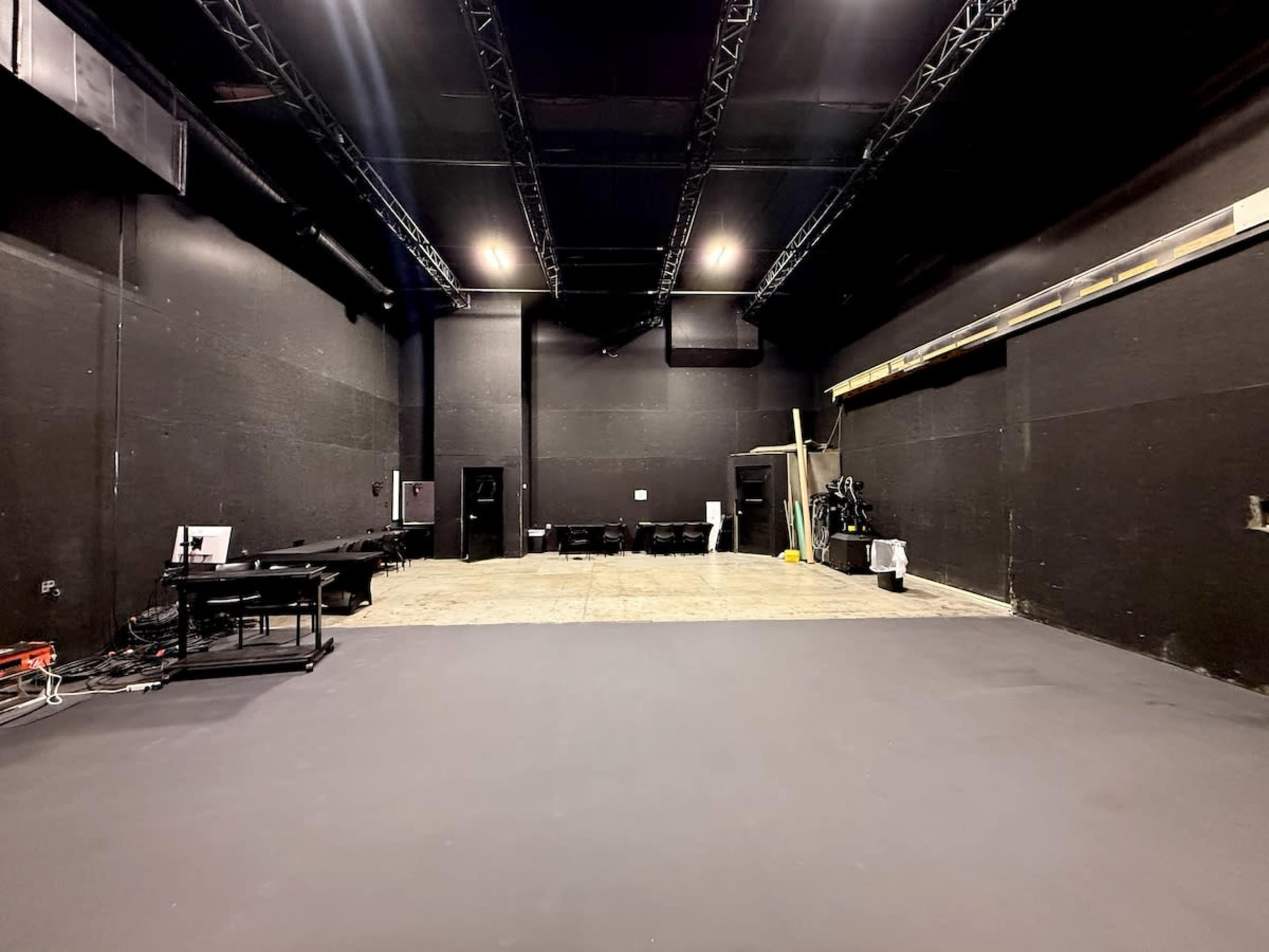 The image shows a large, empty studio space with black walls, a smooth floor, and equipment along the edges.