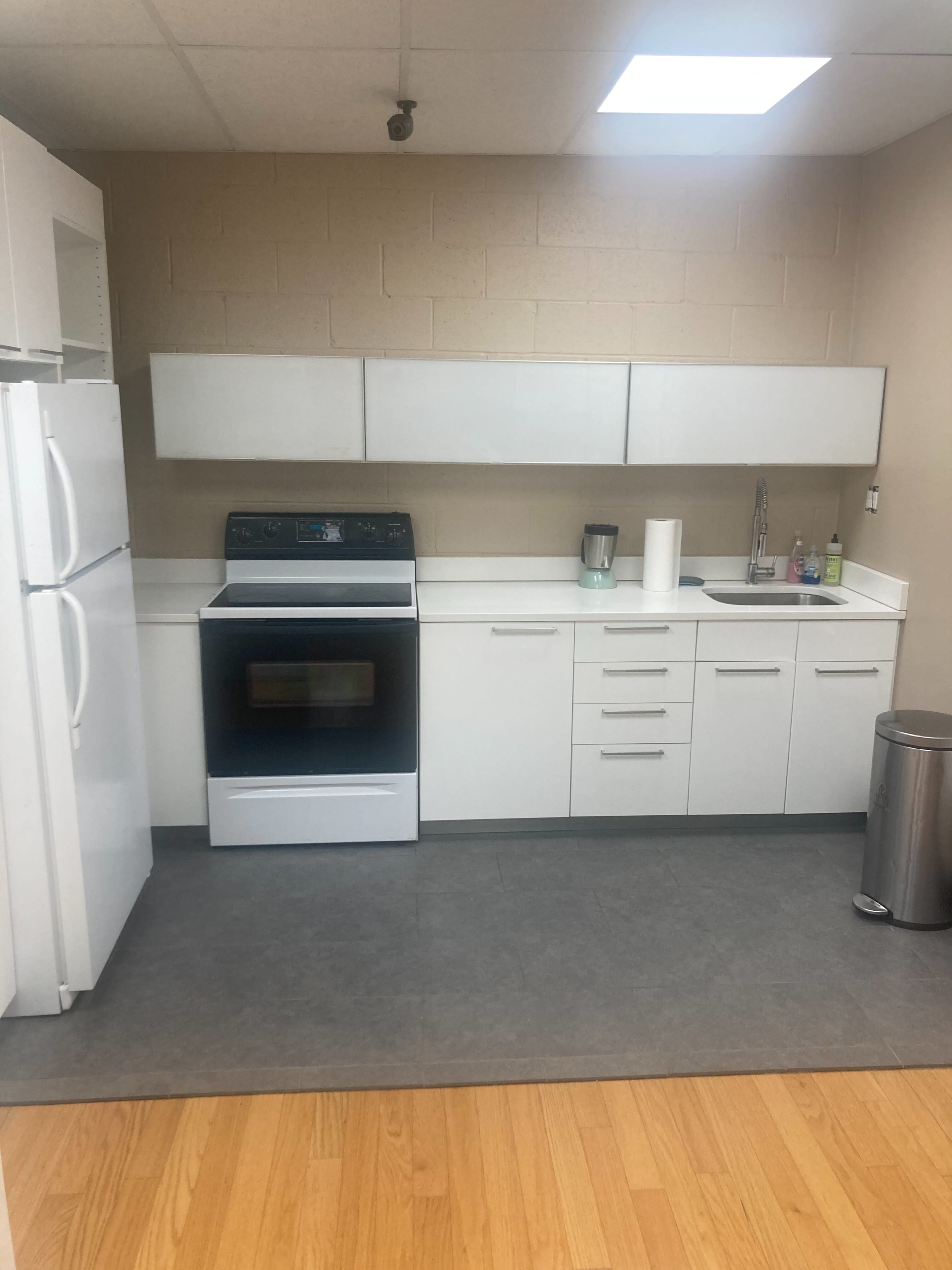 A modern kitchen with white cabinetry, a black oven, and a refrigerator, featuring a sink and minimal countertop appliances.