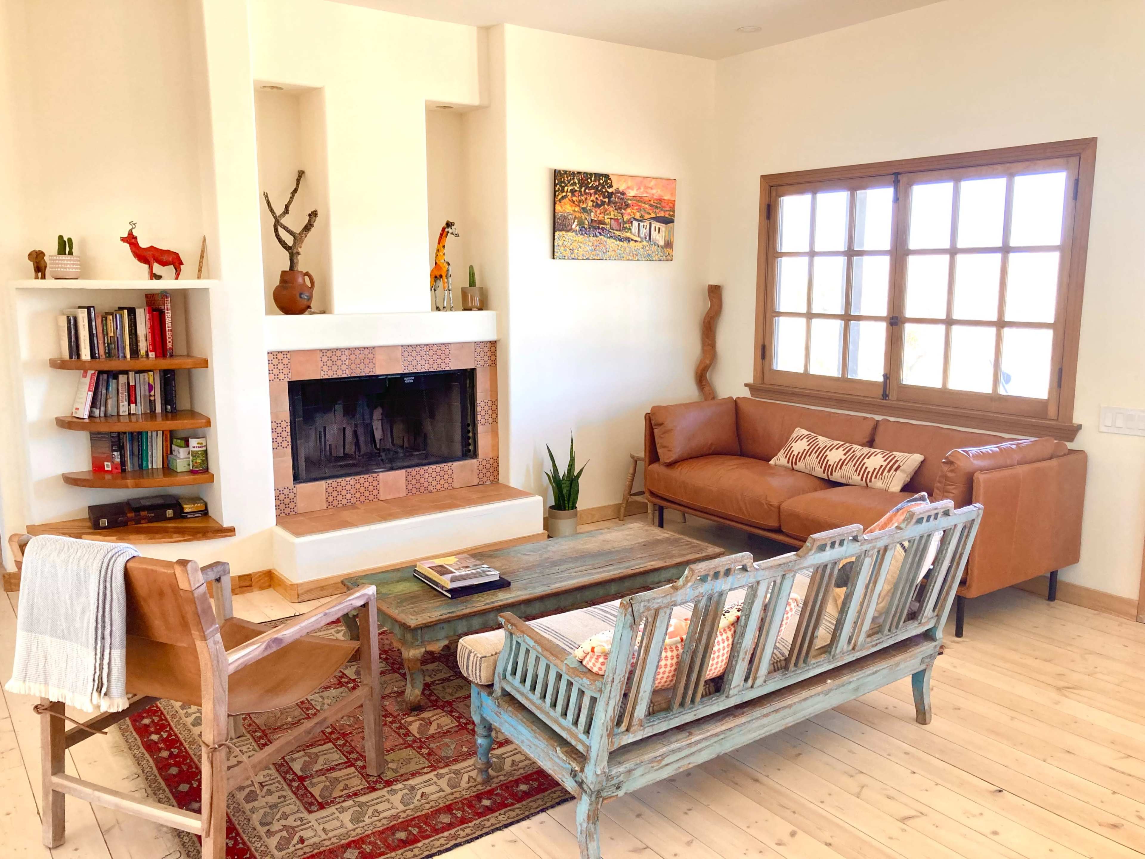 The image shows a well-lit living room with a fireplace, a wooden coffee table, two leather sofas, and a bookshelf filled with books.