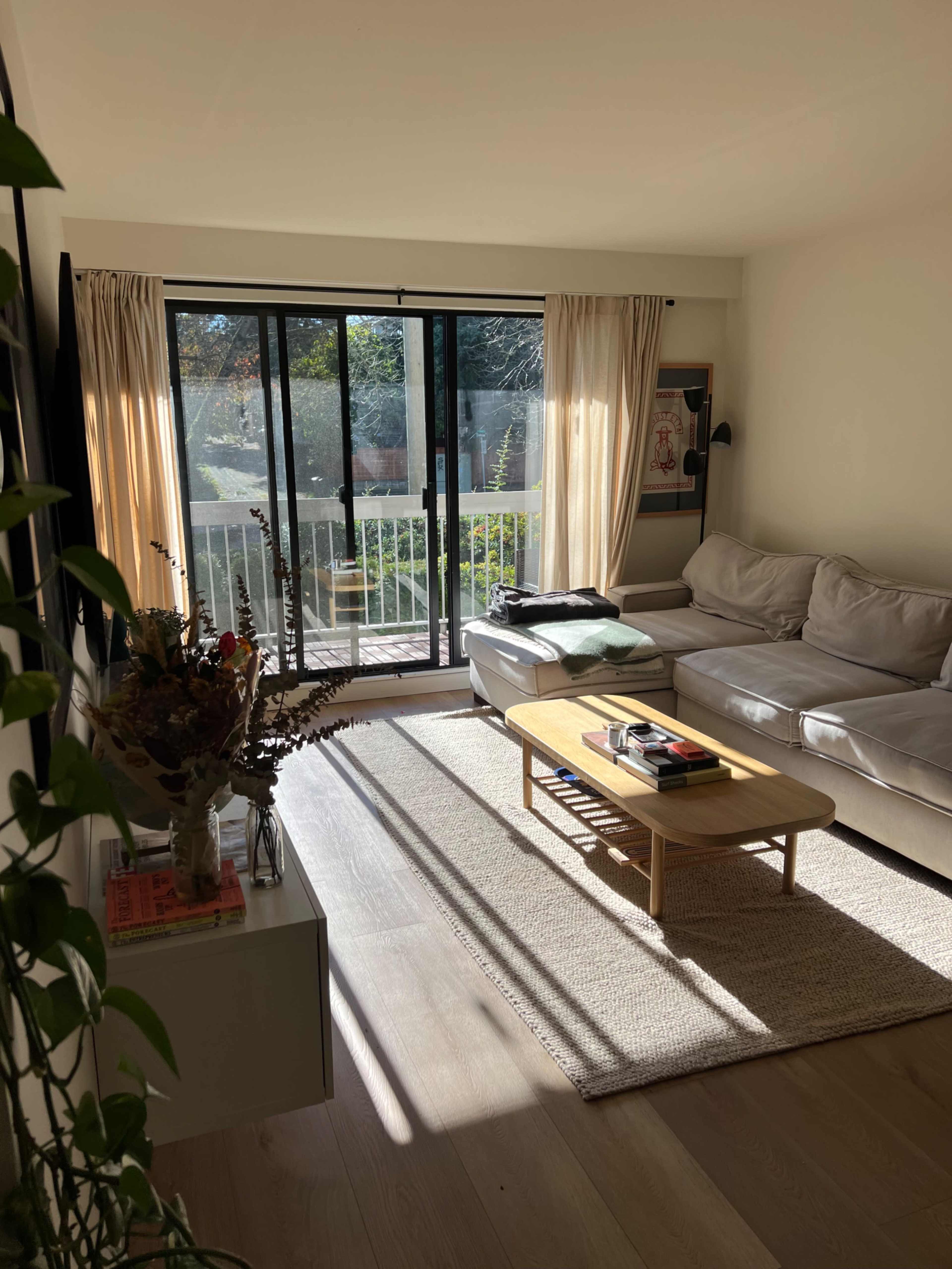 A sunlit living room with a couch, coffee table, and large sliding glass doors leading to a balcony.