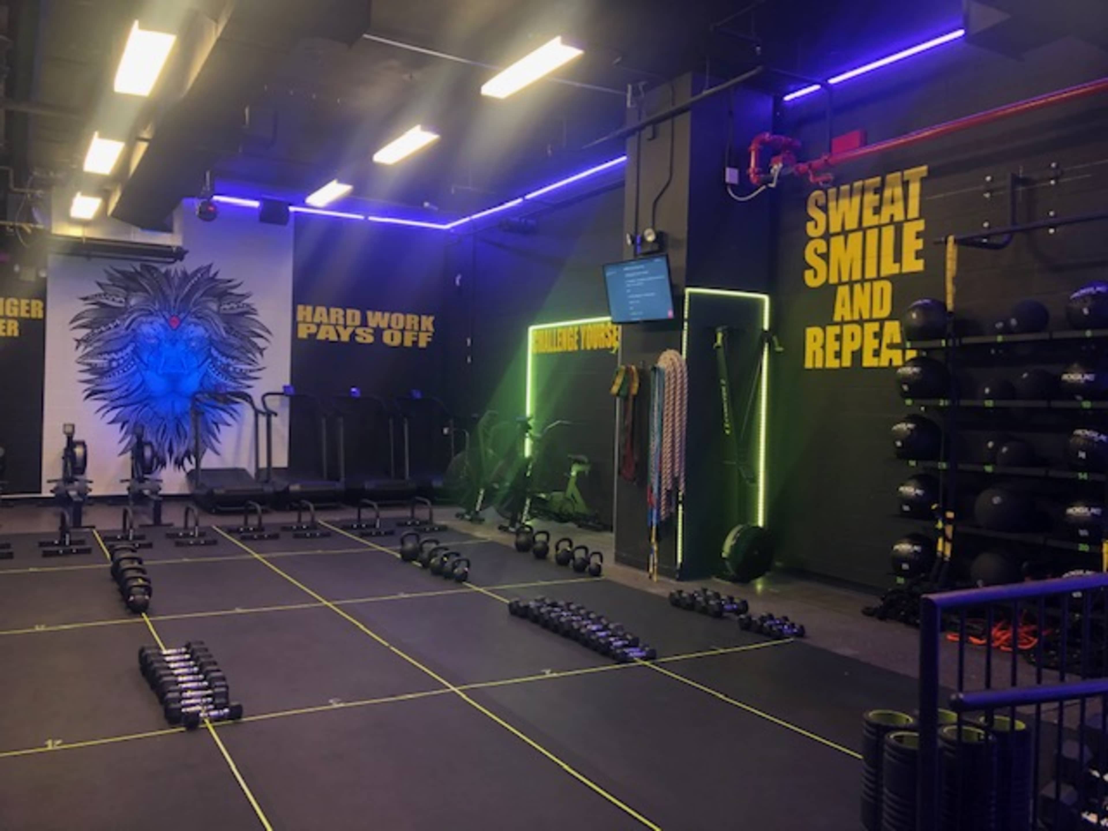 The image shows a fitness studio with exercise equipment arranged on the floor, motivational phrases on the walls, and colorful lighting.