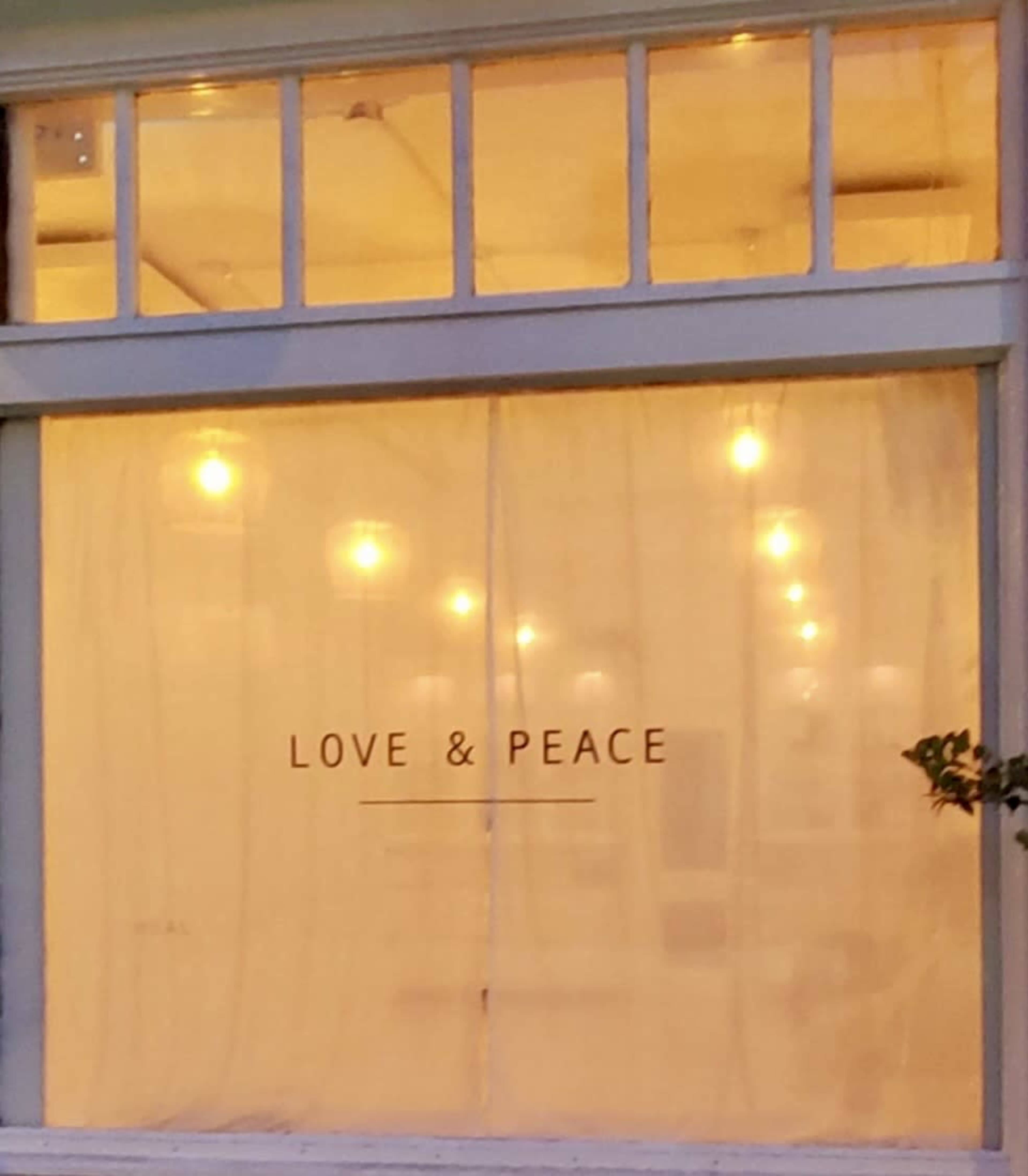 A shop window with sheer curtains displays the words "LOVE & PEACE" in the center.