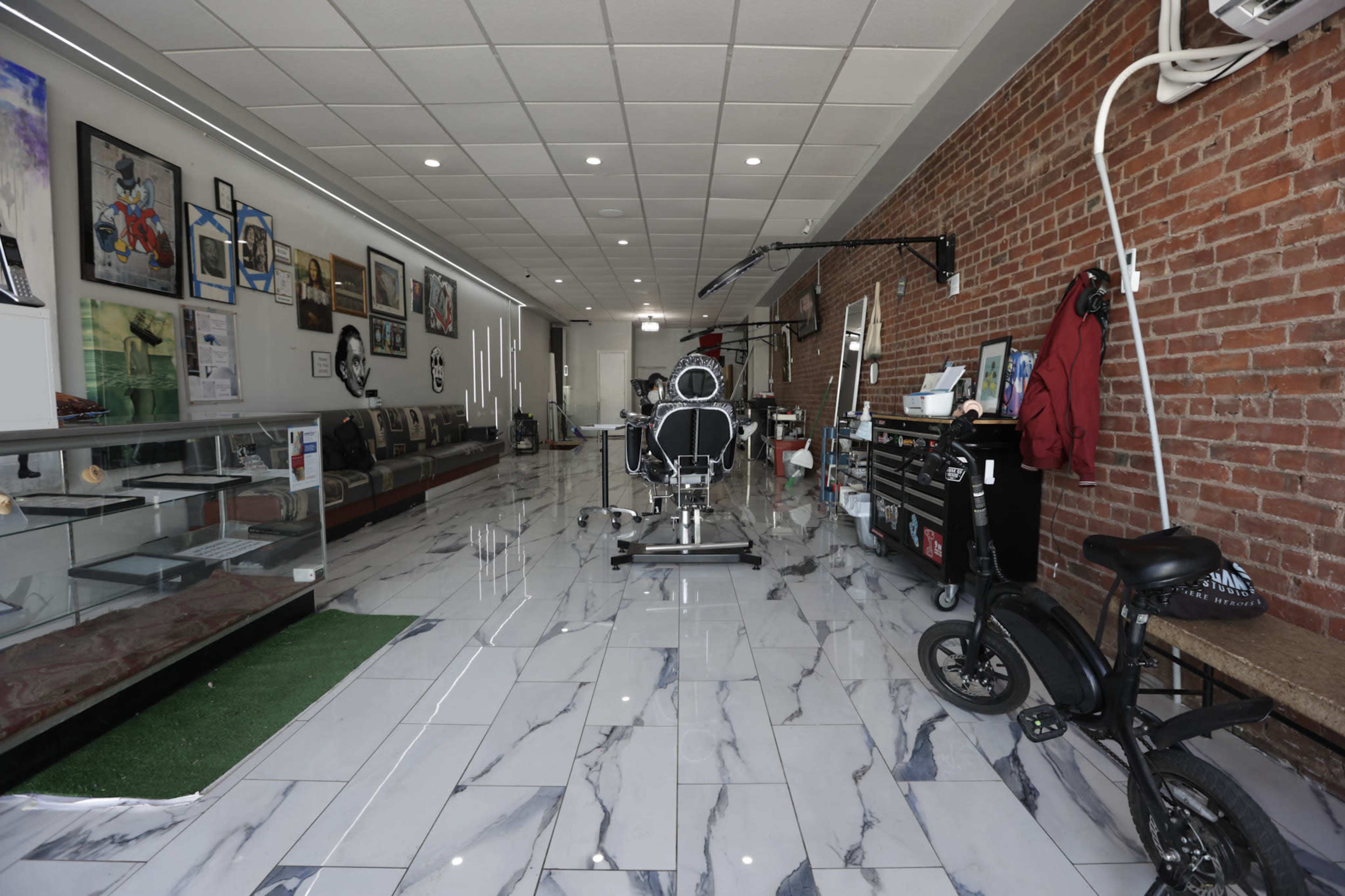 A spacious barbershop with a brick wall, tiled flooring, and various art pieces displayed on the walls.