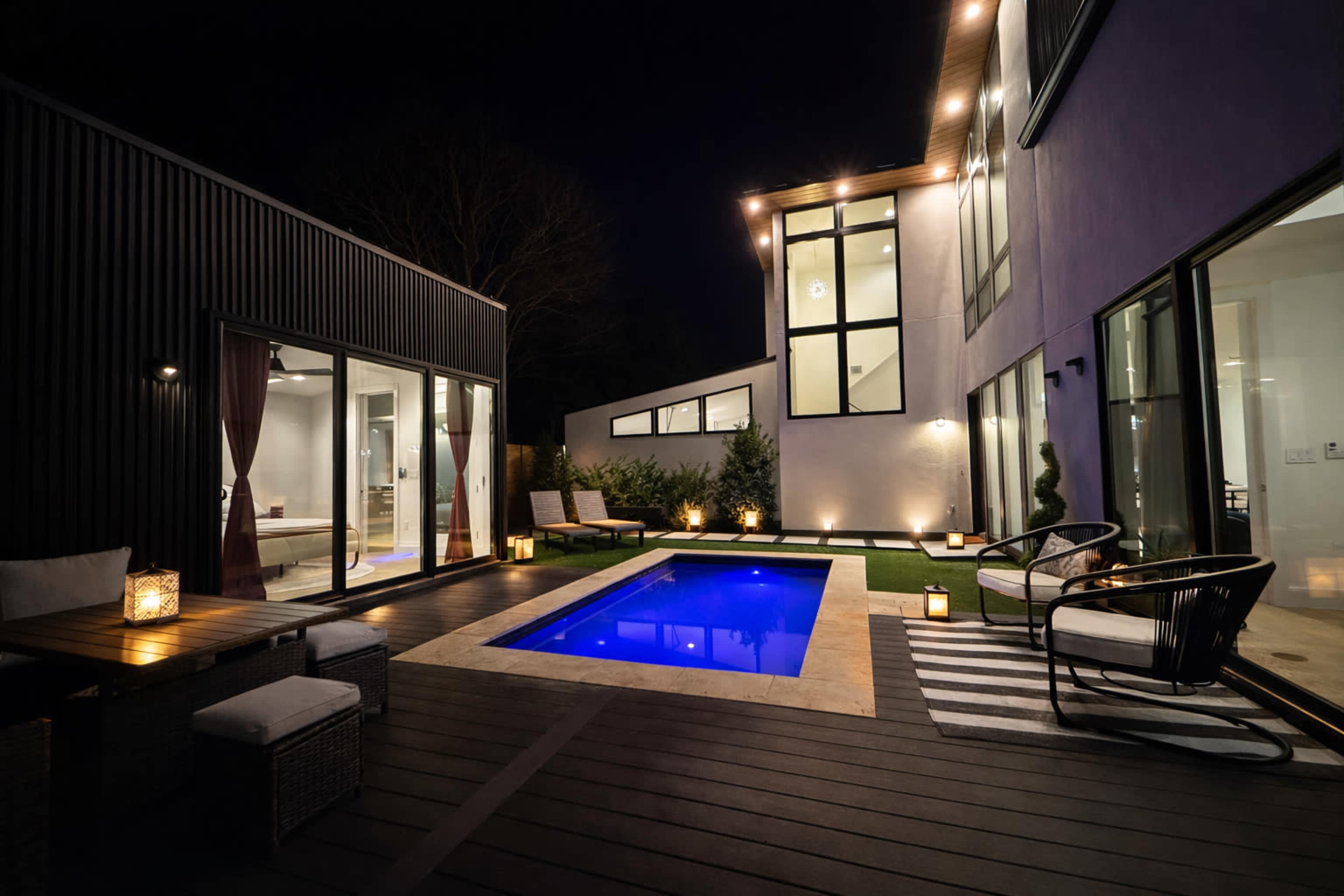 A modern backyard features a small illuminated pool surrounded by comfortable seating and decorative lanterns at night.