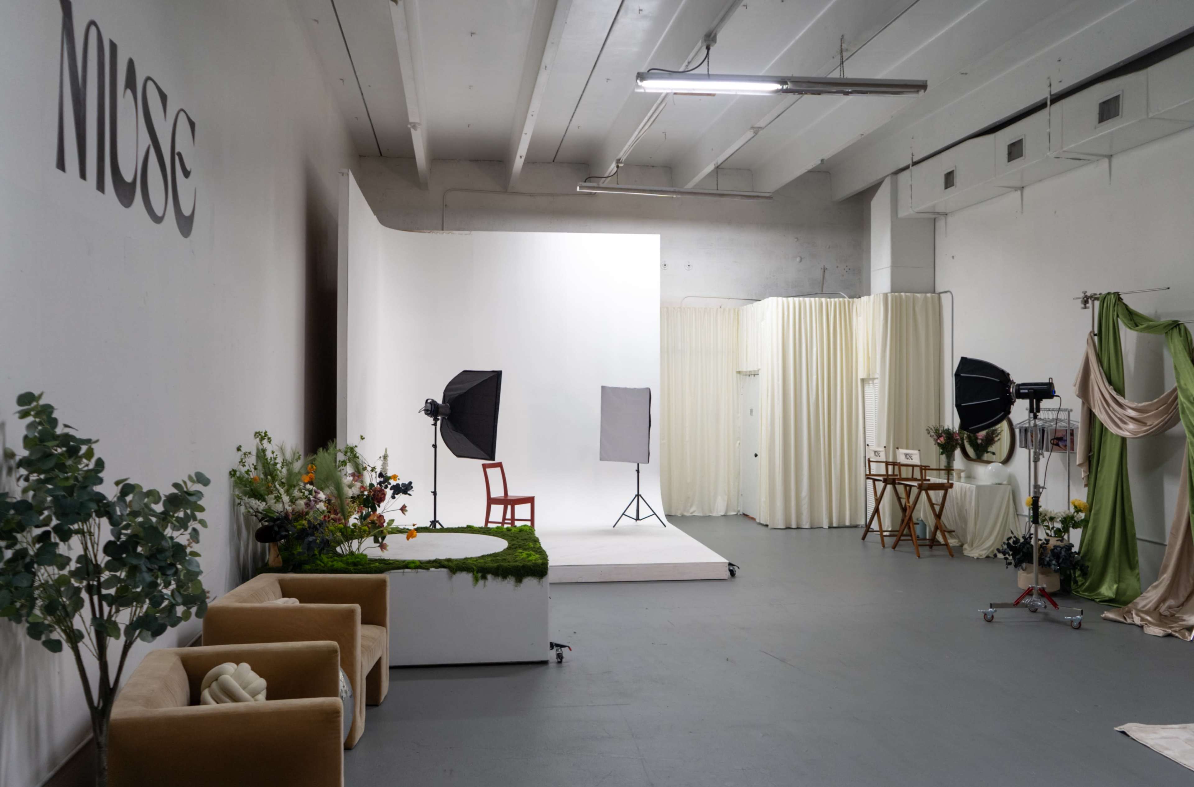 The image shows a spacious photo studio with various backdrops, lighting equipment, and a seating area.