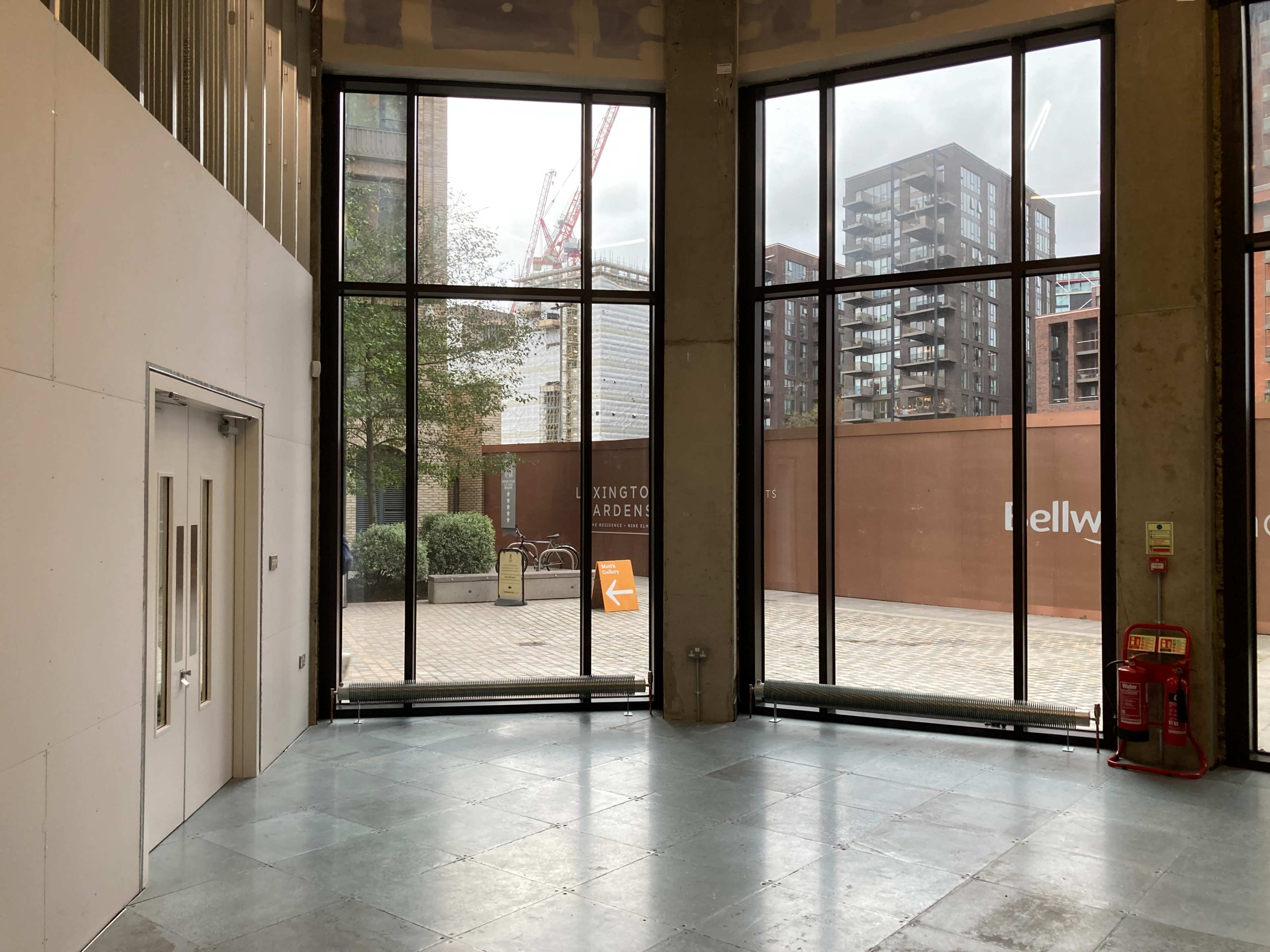 A spacious interior with large glass windows overlooking a paved outdoor area and modern buildings.