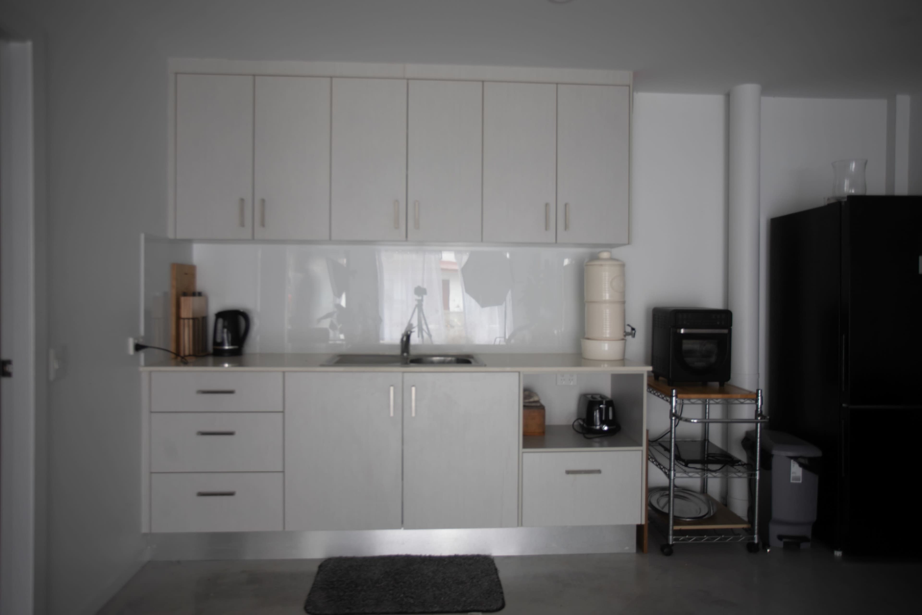The image shows a modern kitchen featuring light-colored cabinets, a stainless steel sink, and various kitchen appliances, including a kettle and a coffee maker.