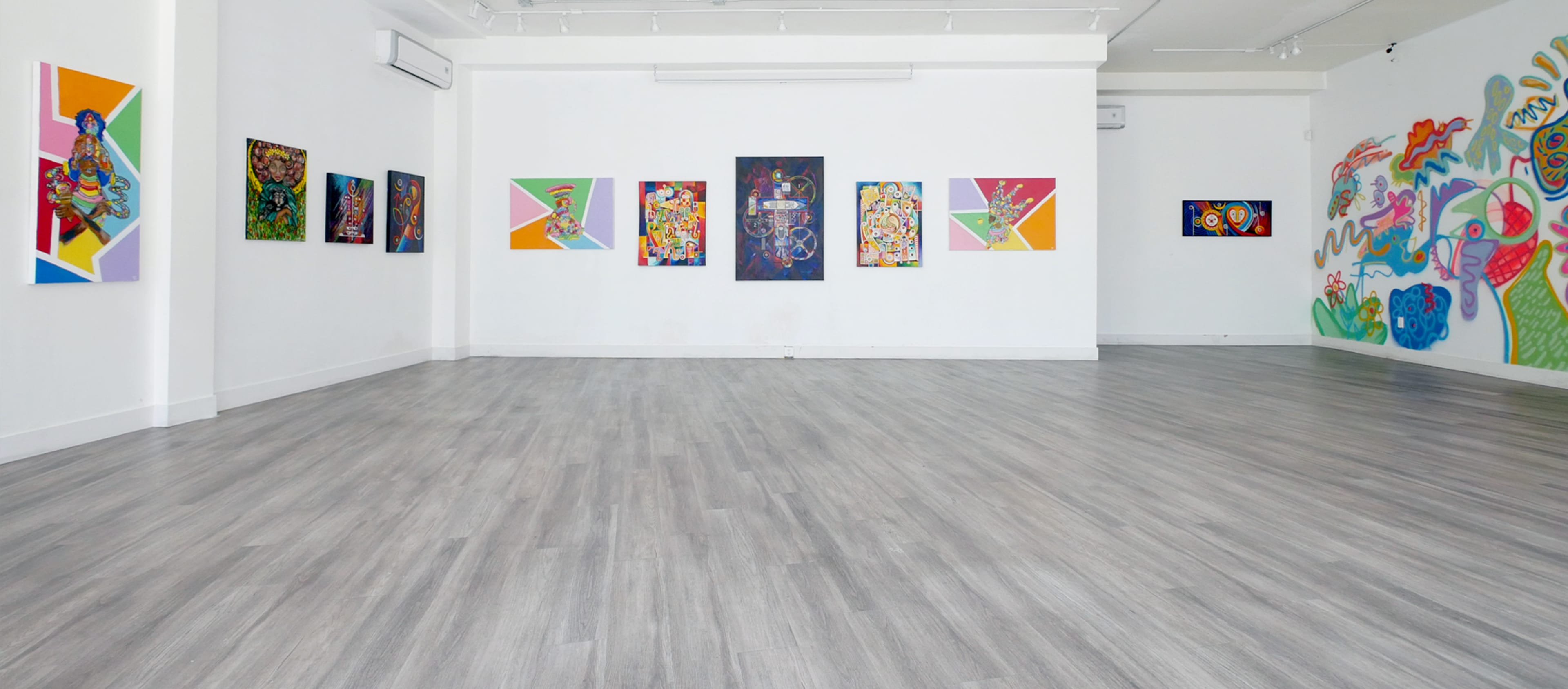 A brightly lit art gallery featuring colorful paintings on the walls and a spacious wooden floor.