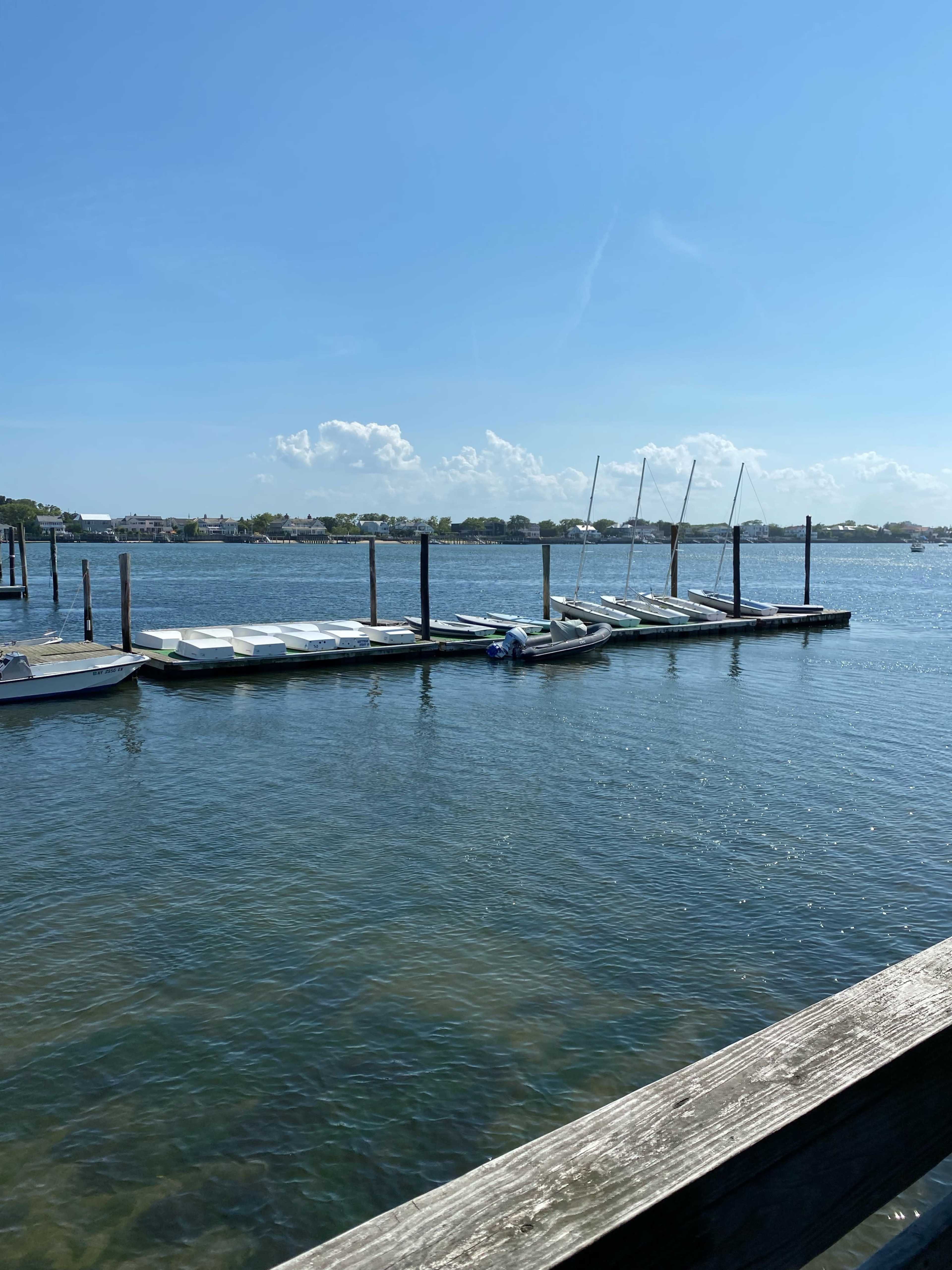 The image shows a dock with several boats moored alongside a calm body of water under a clear blue sky.