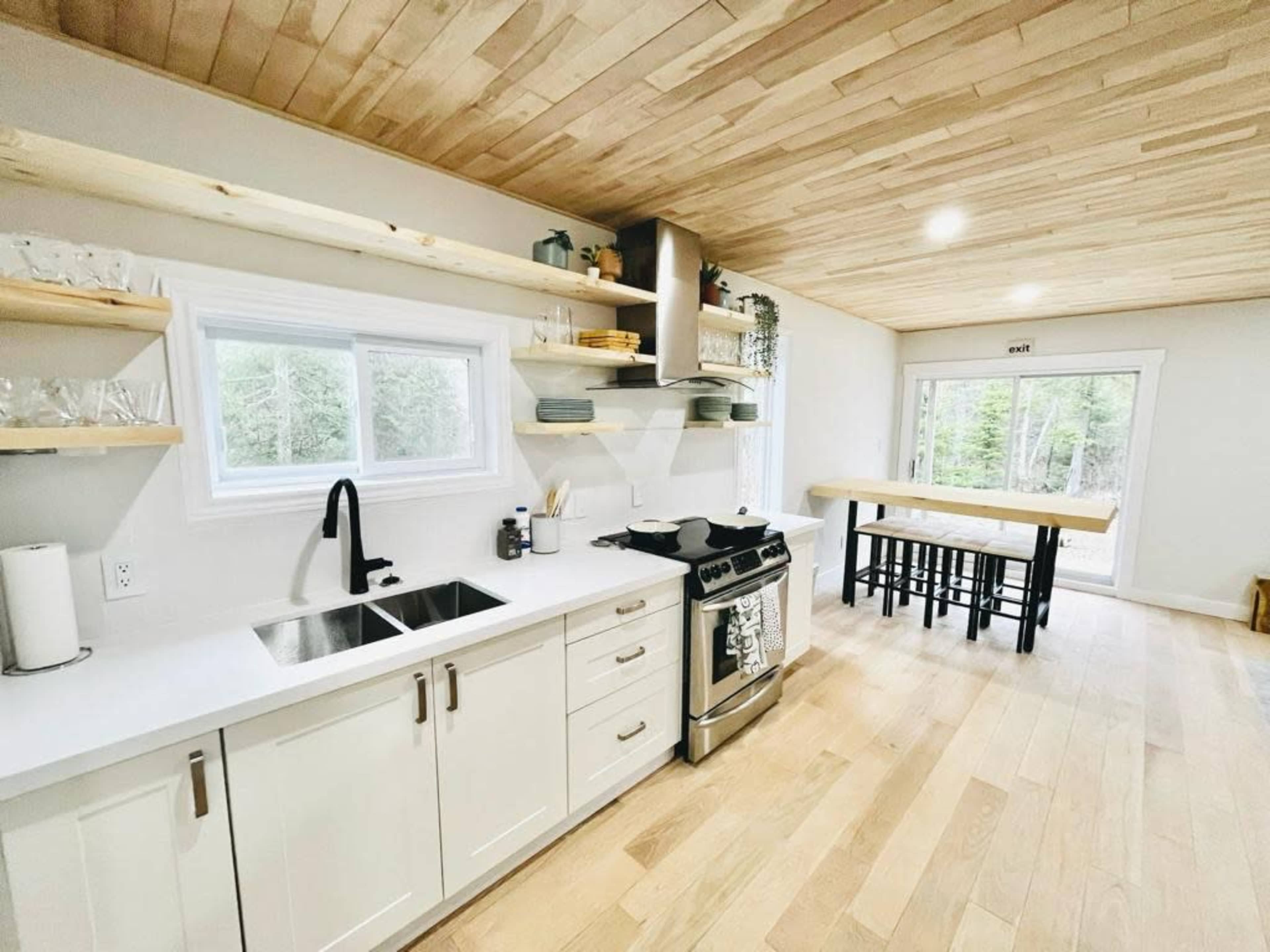 The kitchen features modern cabinets, a stainless steel stove, and an island table with bar stools, all under a wooden ceiling.