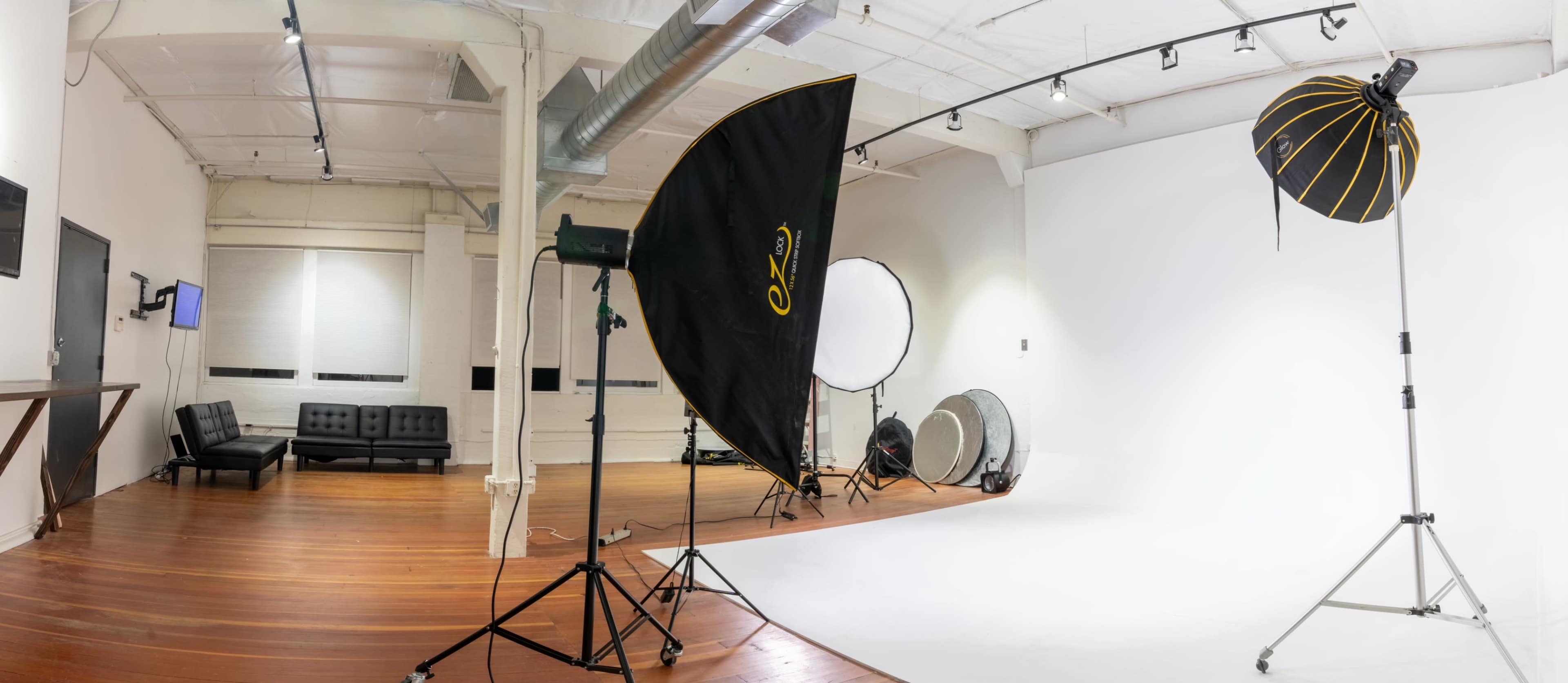A photography studio with a white backdrop, lighting equipment, and a seating area.