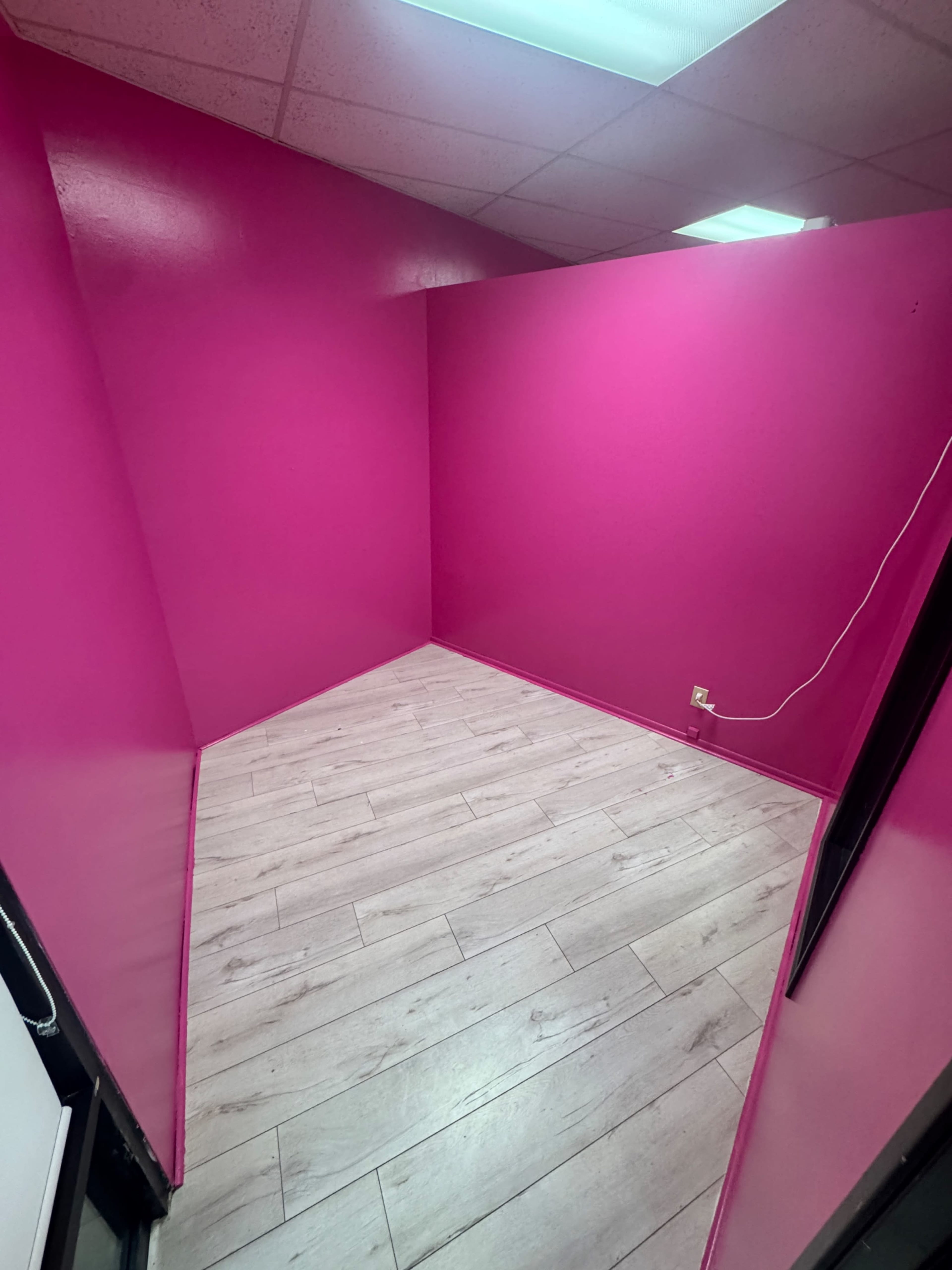 The image shows an empty room with bright pink walls and light-colored wooden flooring.