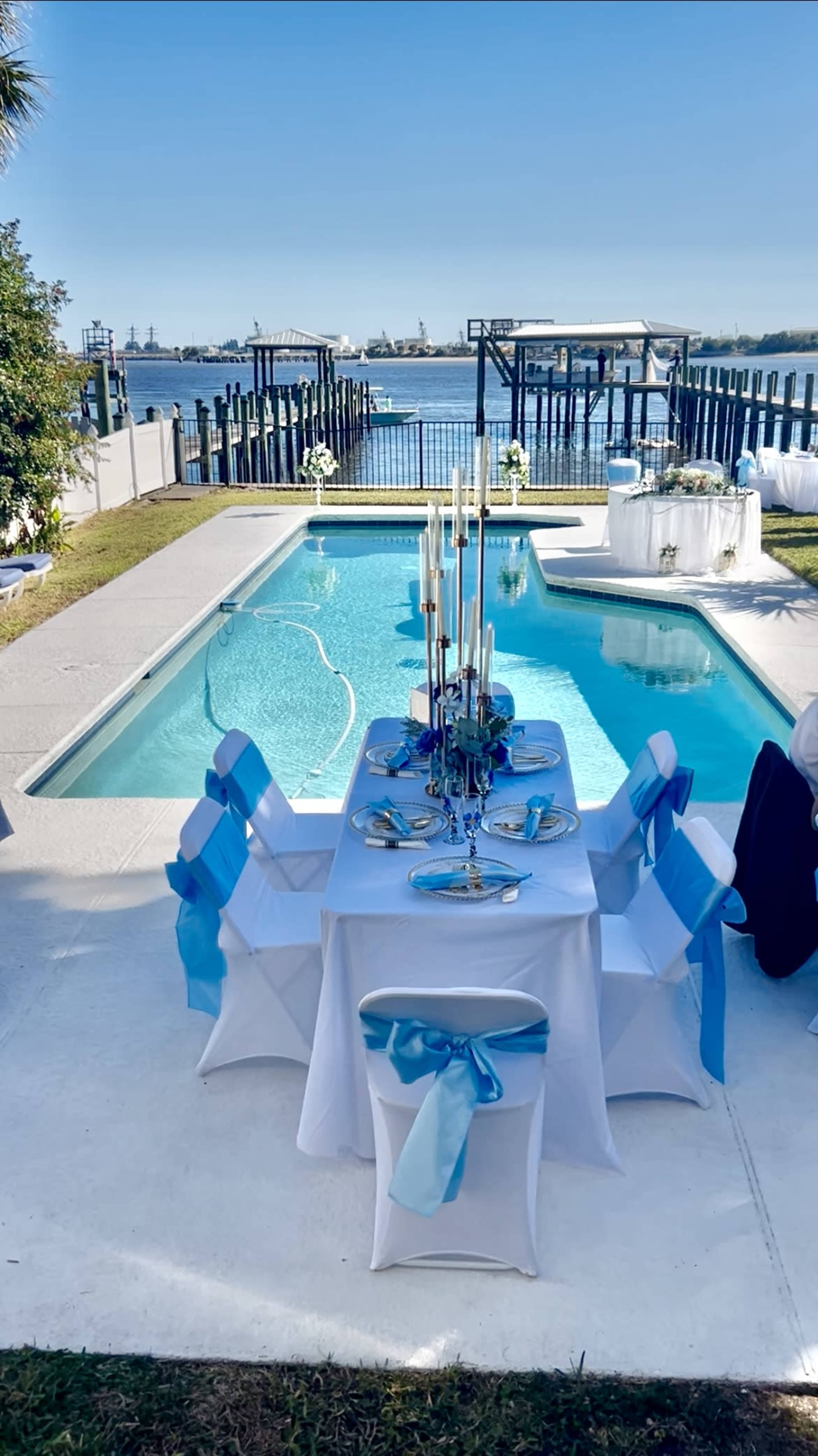 A beautifully arranged outdoor dining setup with a poolside view overlooking a body of water and decorated with blue accents.