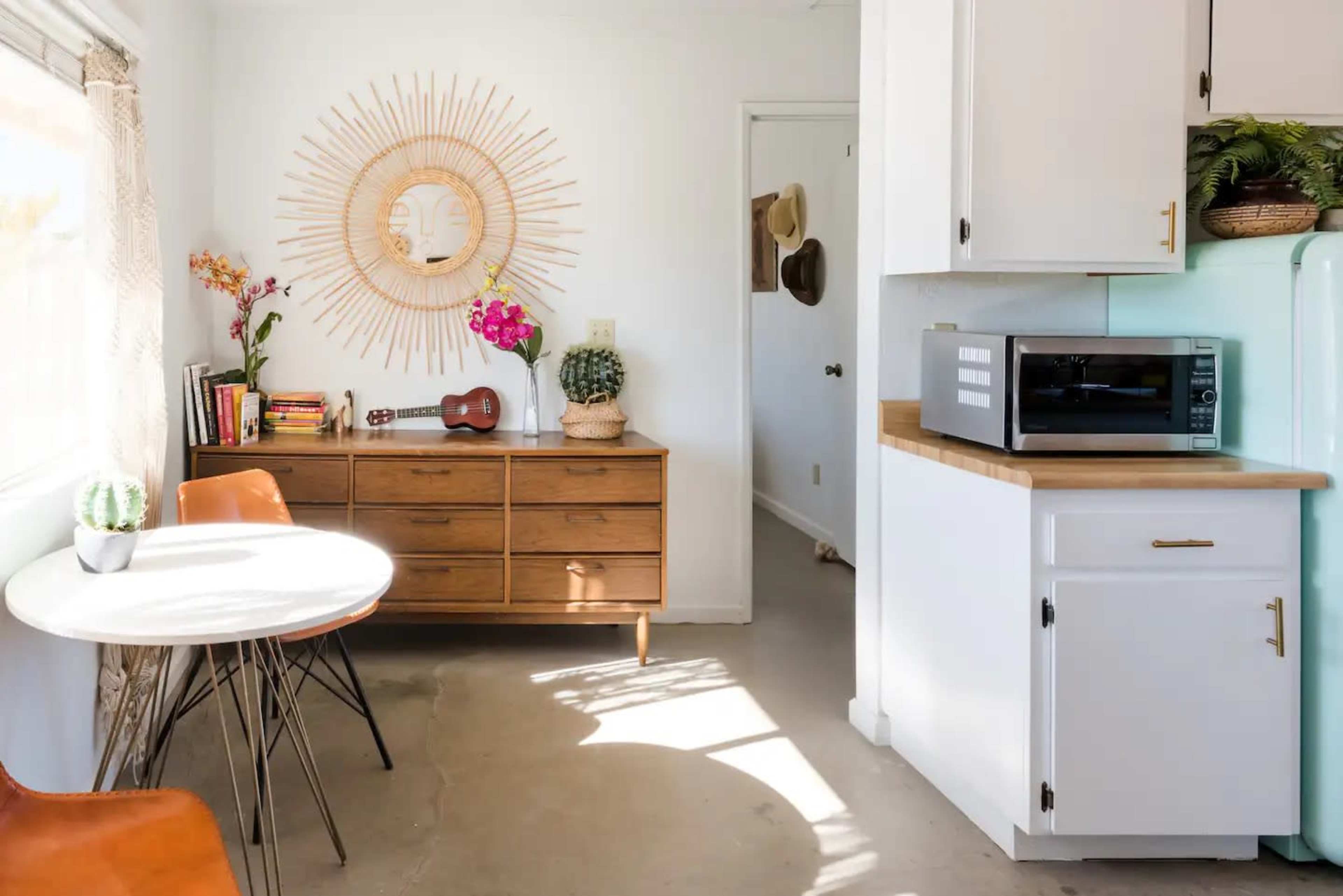 A light-filled kitchen features a round dining table, wooden dresser, and a small appliance area with a microwave and retro-style refrigerator.