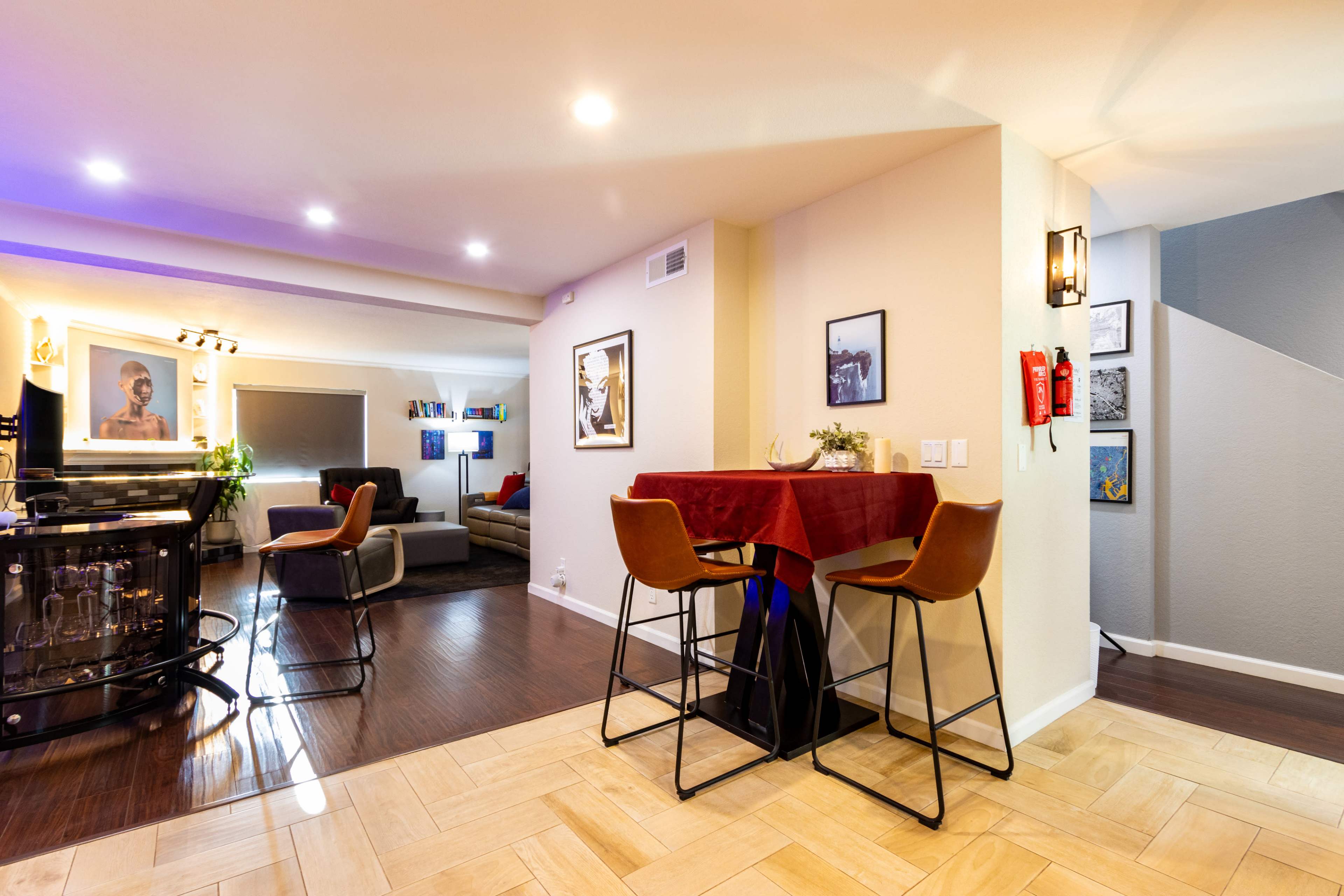 A modern living space with a dining area featuring two chairs and a small table, leading to a cozy seating area with artwork on the walls.