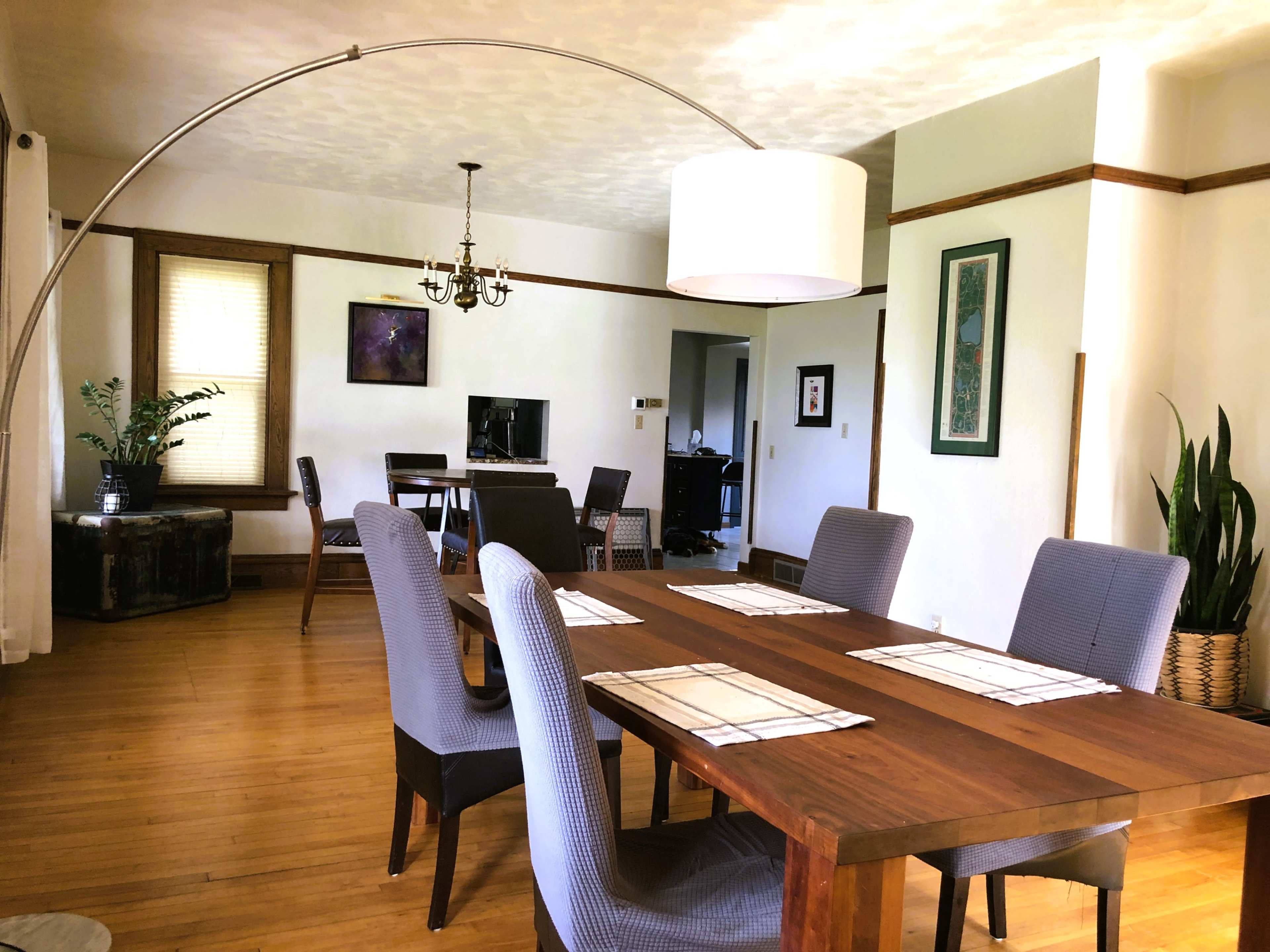 A spacious dining area with a wooden table, upholstered chairs, an arc floor lamp, and a view of a connected living space.