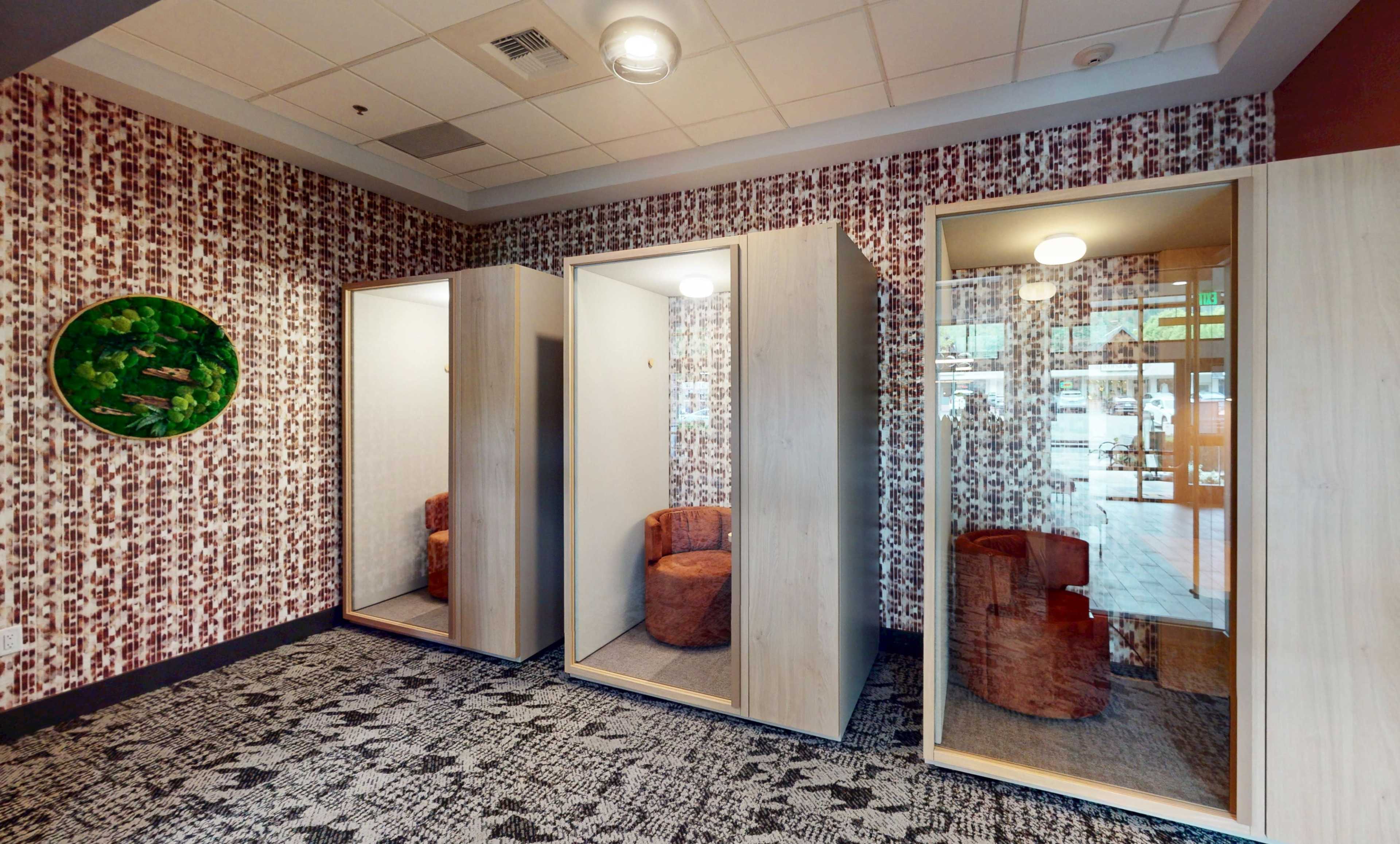 The image shows a modern waiting area featuring three individual booths with mirrors and circular seats, set against a patterned wall.