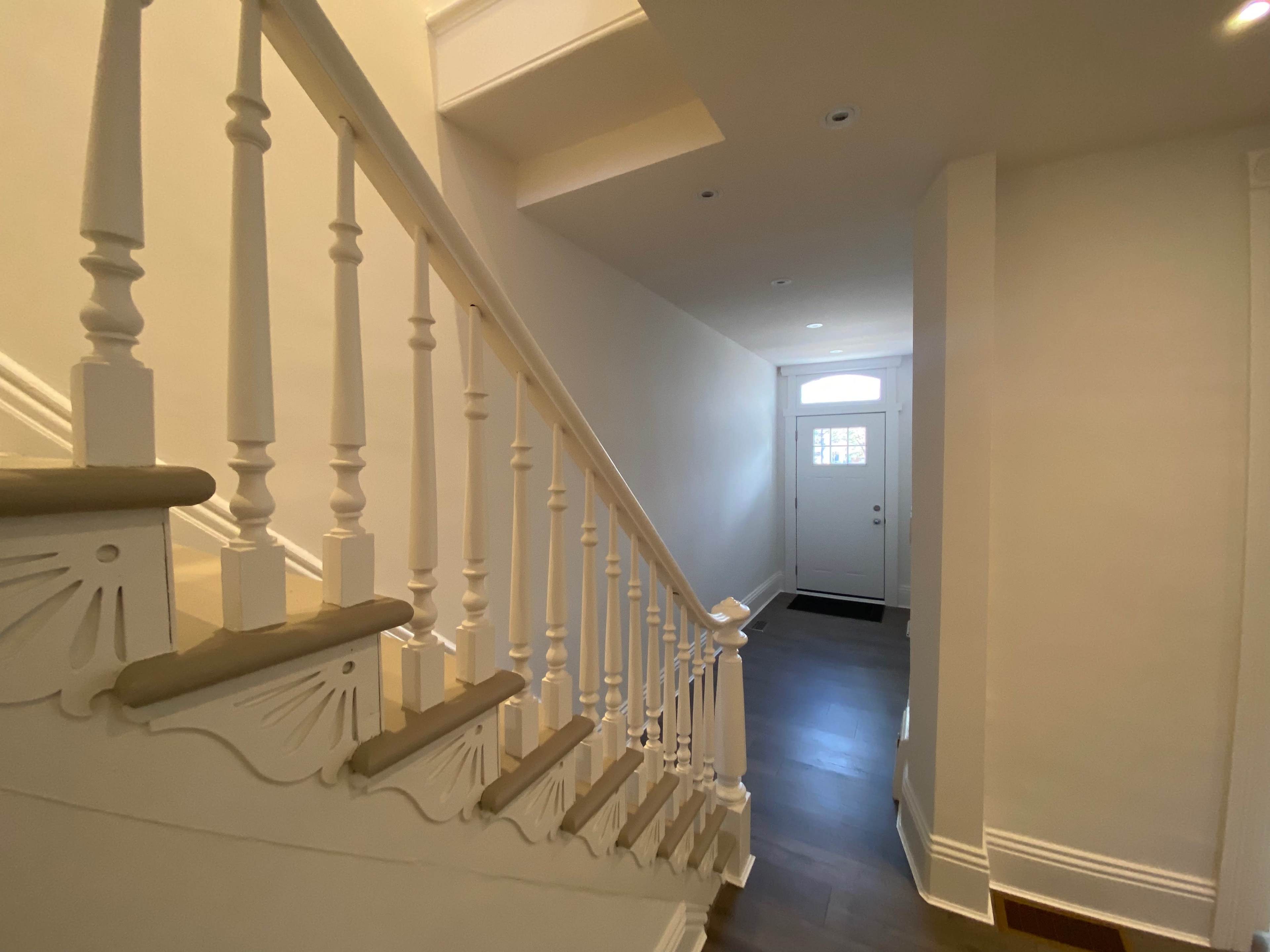 A well-lit staircase with white balustrades leading to a hallway and a front door at the end.
