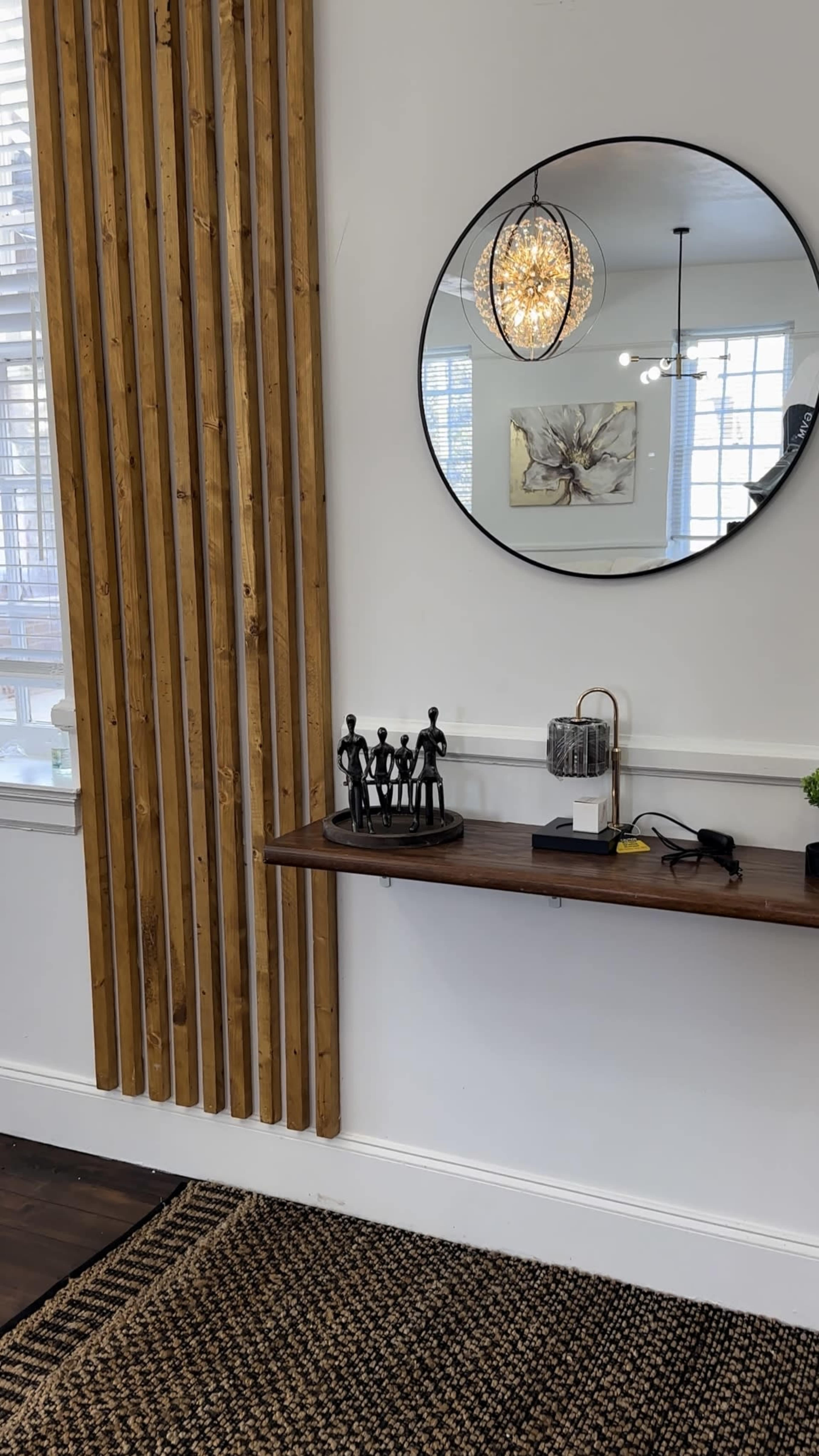 The image shows a wall with wooden slats, a round mirror, a pendant light, and a shelf displaying various decorative items.