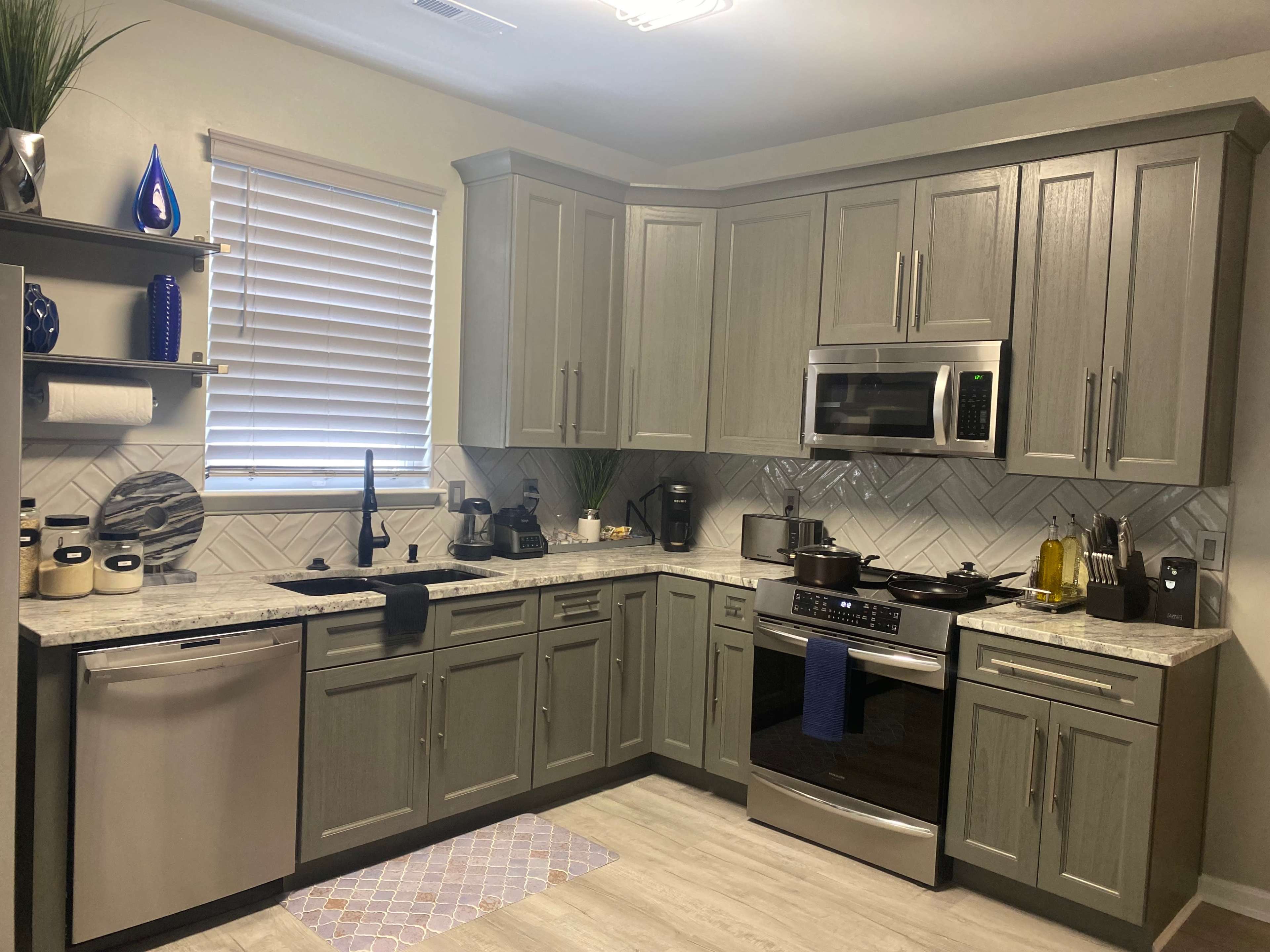 The image shows a modern kitchen with gray cabinets, stainless steel appliances, and a patterned backsplash.