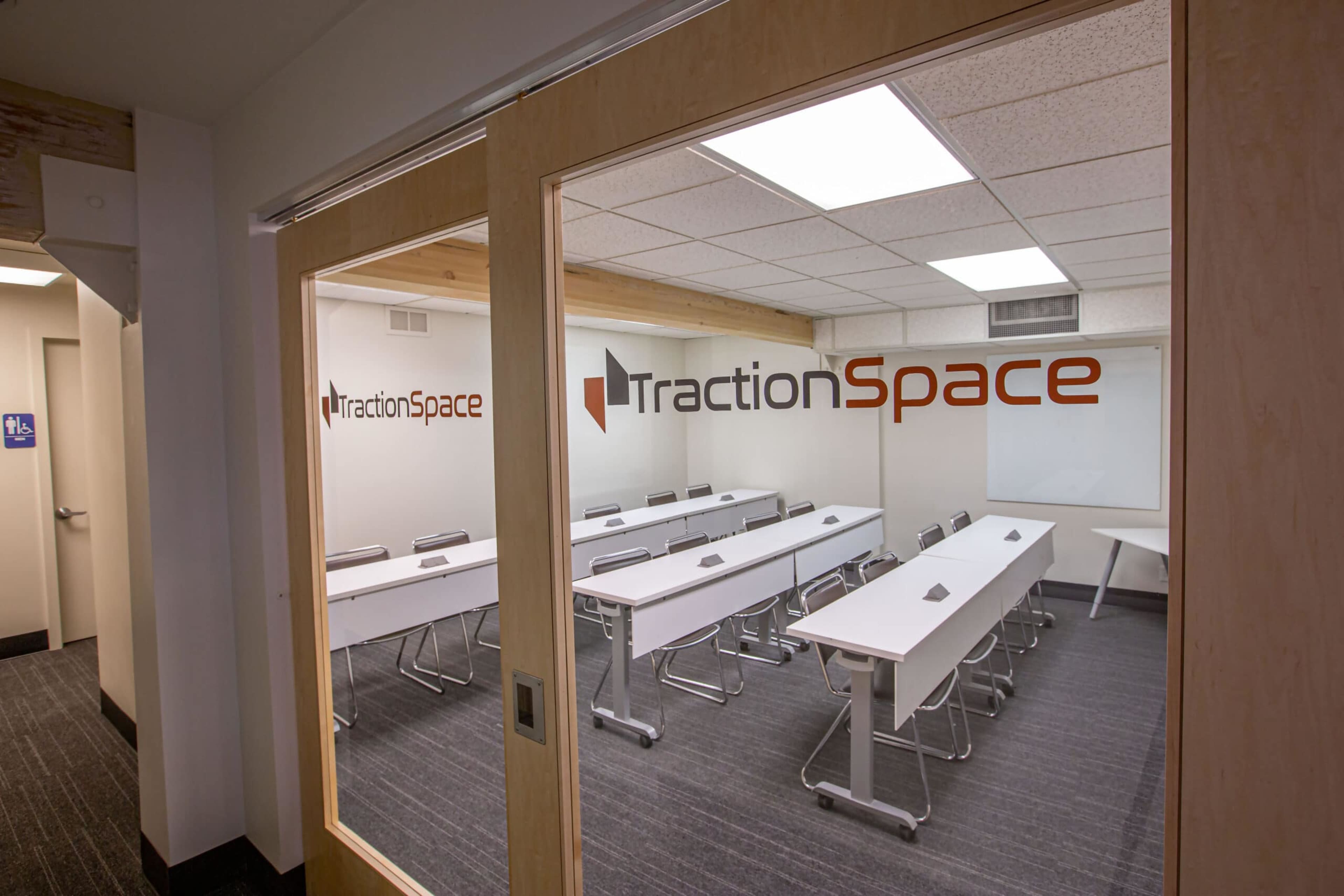 A conference room with multiple white tables arranged in rows and a presentation screen on the front wall.