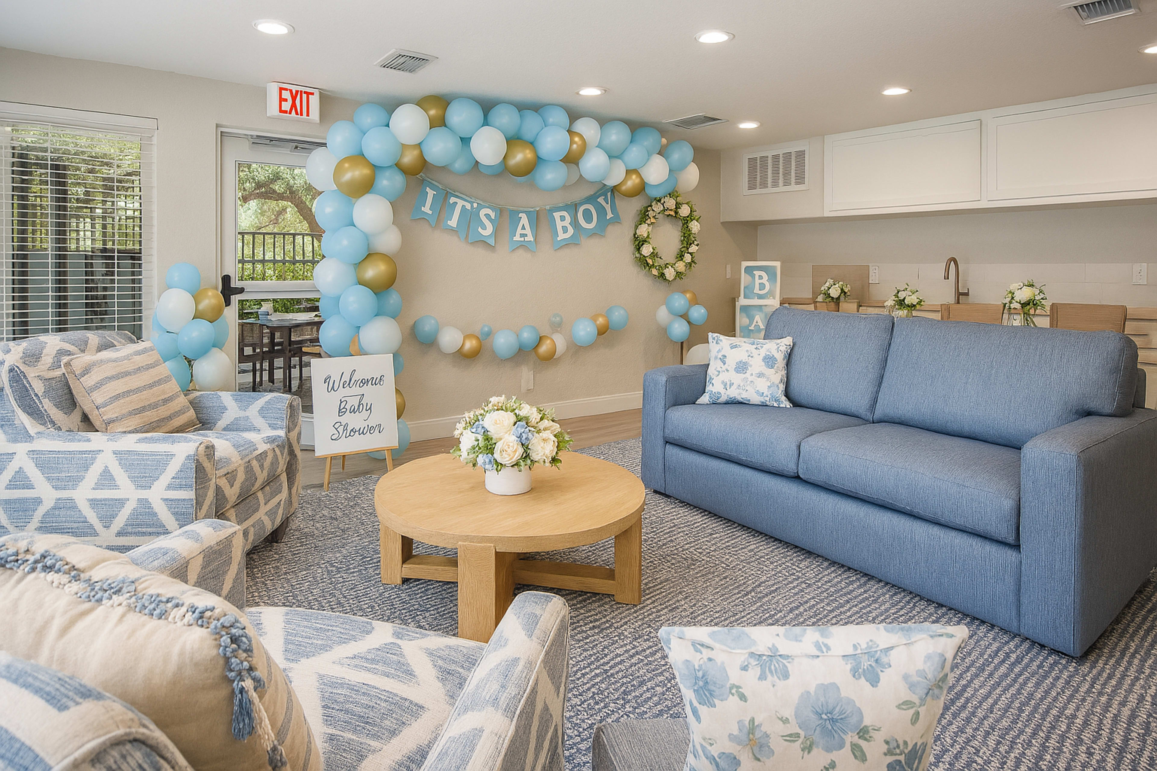 The image shows a cozy room decorated for a baby shower, featuring blue and gold balloon arrangements, a sofa, chairs, and a sign that reads "Welcome Baby Shower."
