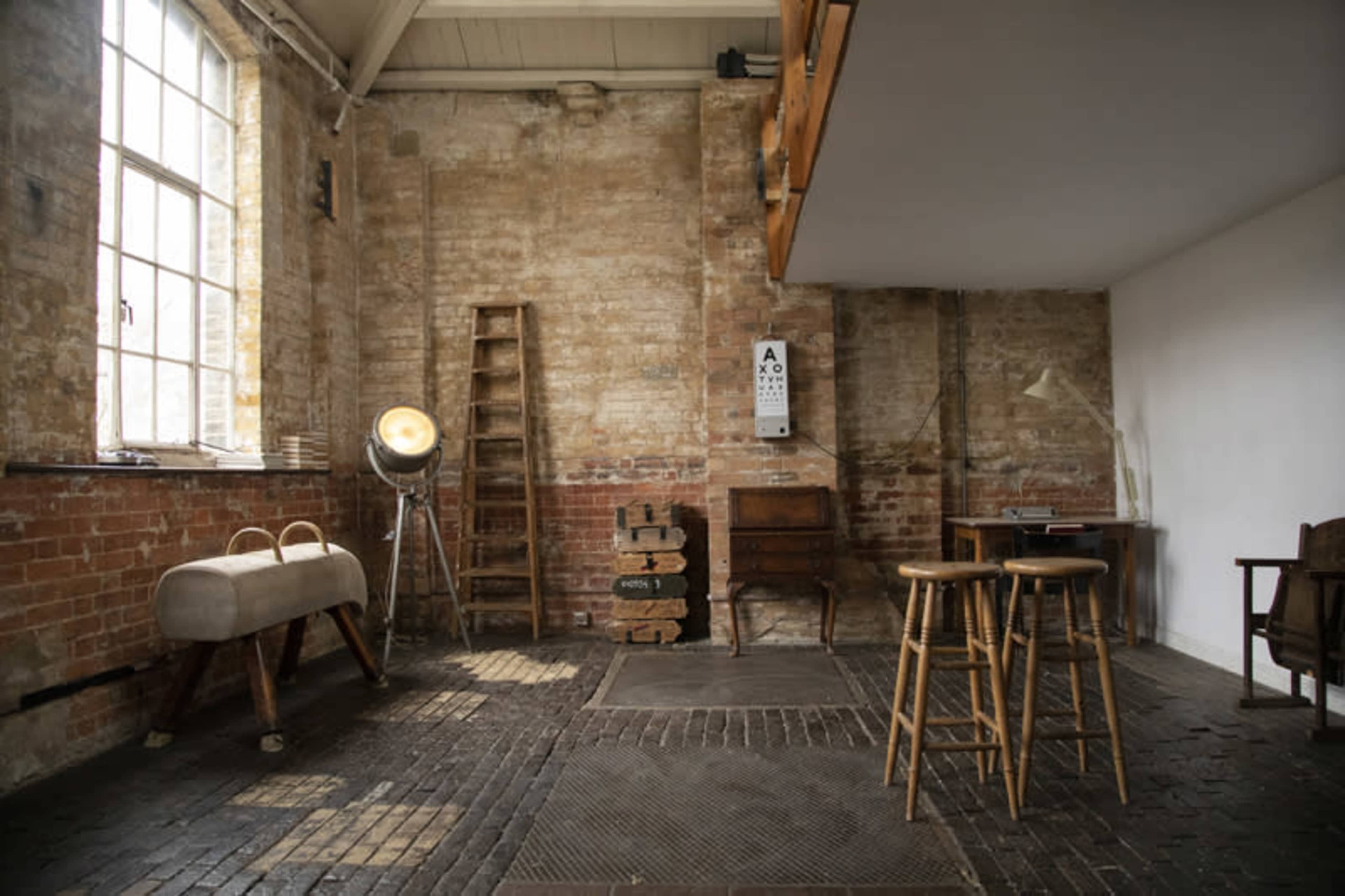 A spacious, industrial-style room with exposed brick walls, wooden furniture, and a large window allowing natural light to enter.