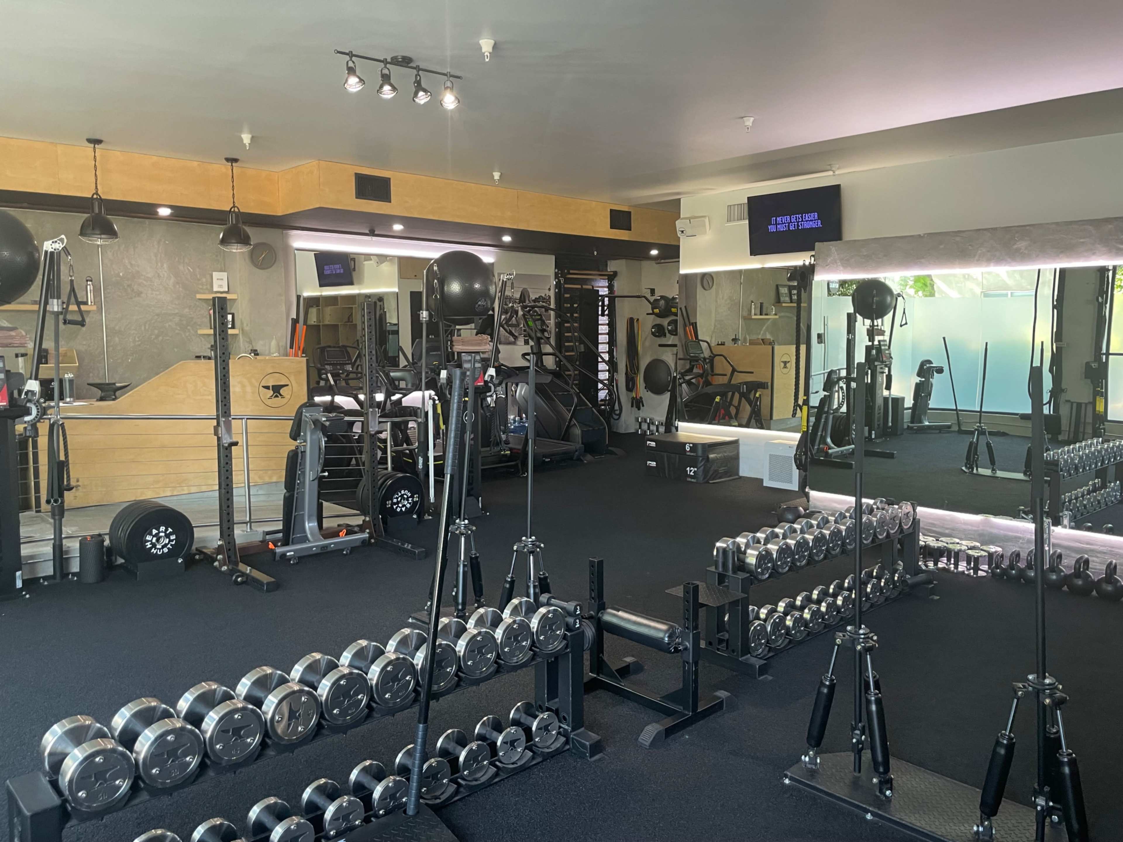 A gym interior equipped with various fitness equipment, including dumbbells, weight machines, and mirrors.