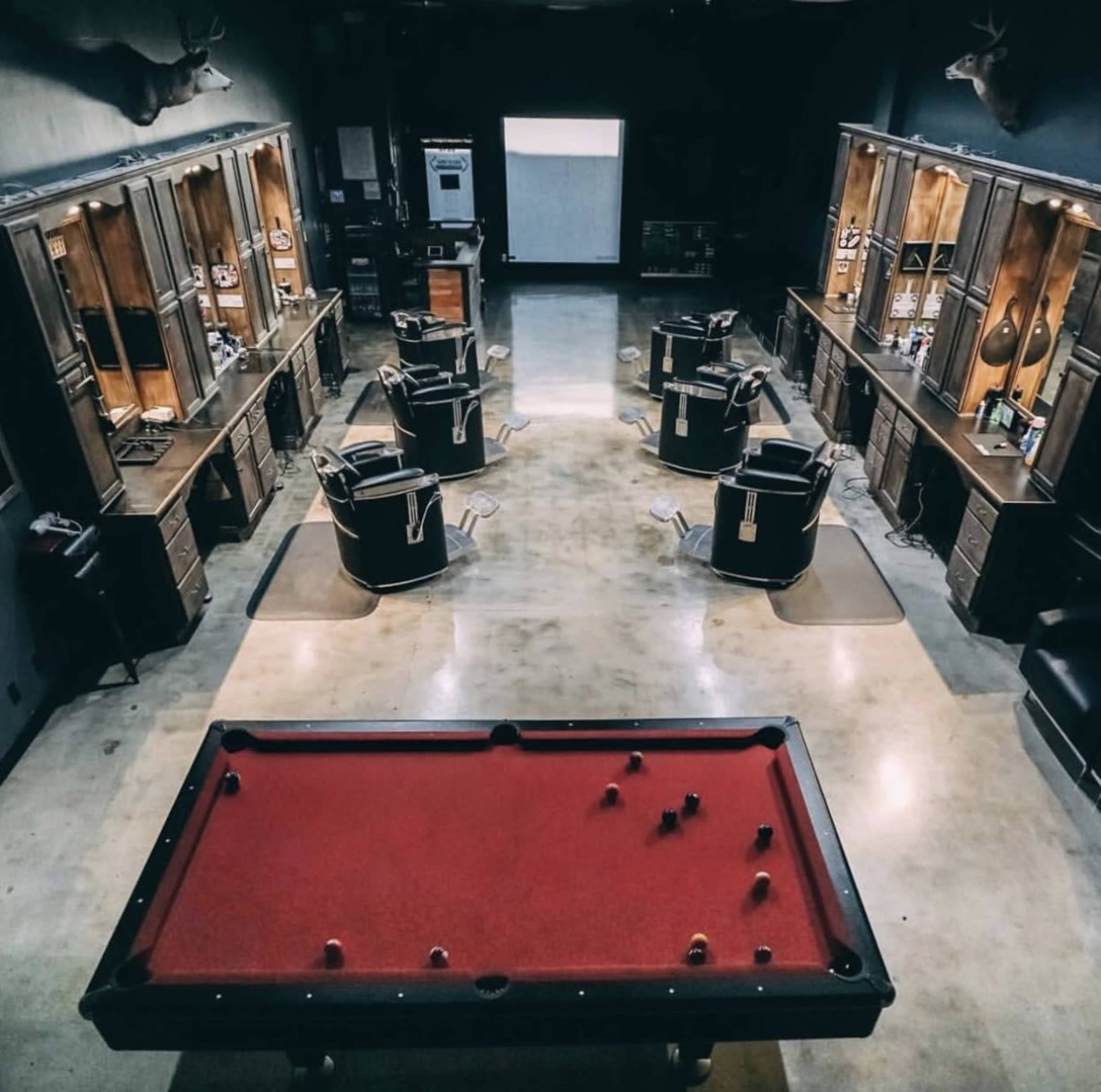 A vintage barbershop interior with several barber chairs, a pool table, and wooden cabinetry lining the walls.