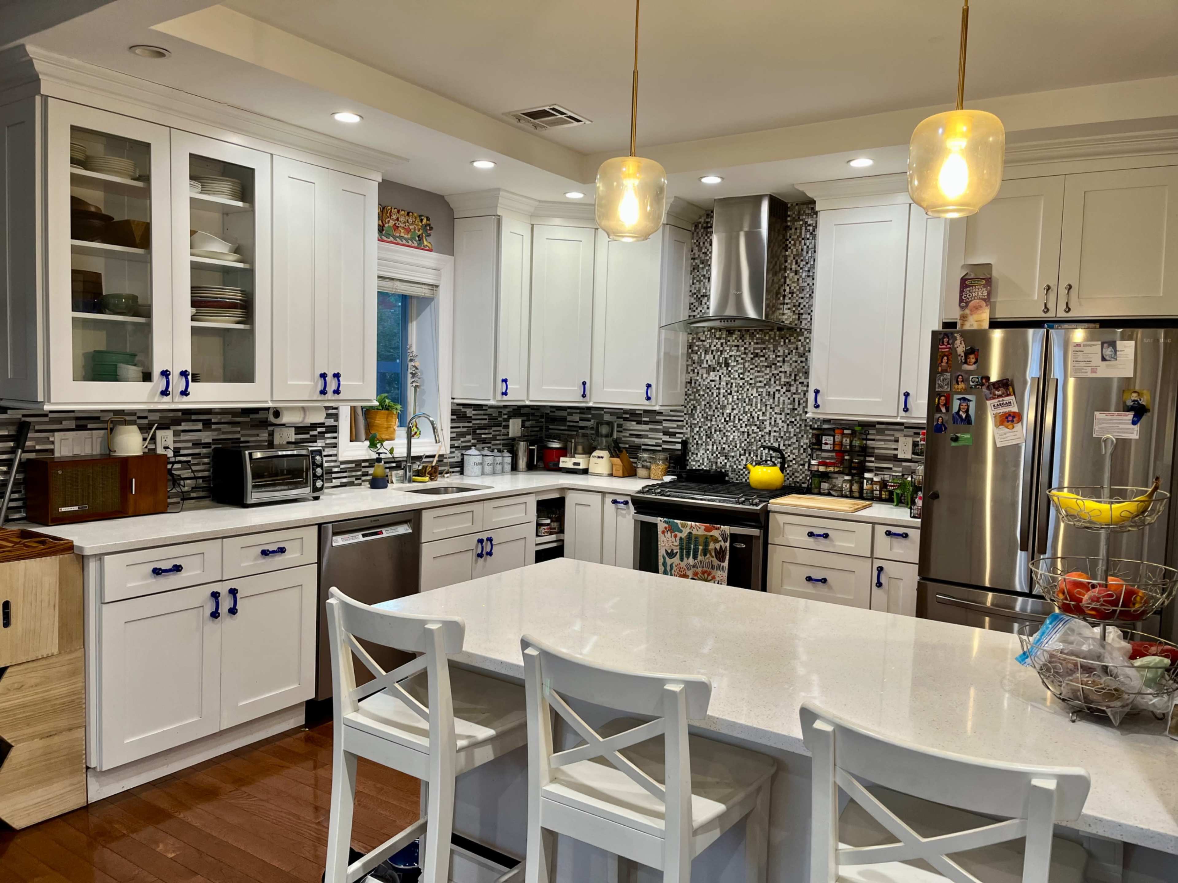 A modern kitchen with white cabinets, a central island with seating, and stainless steel appliances against a decorative backsplash.