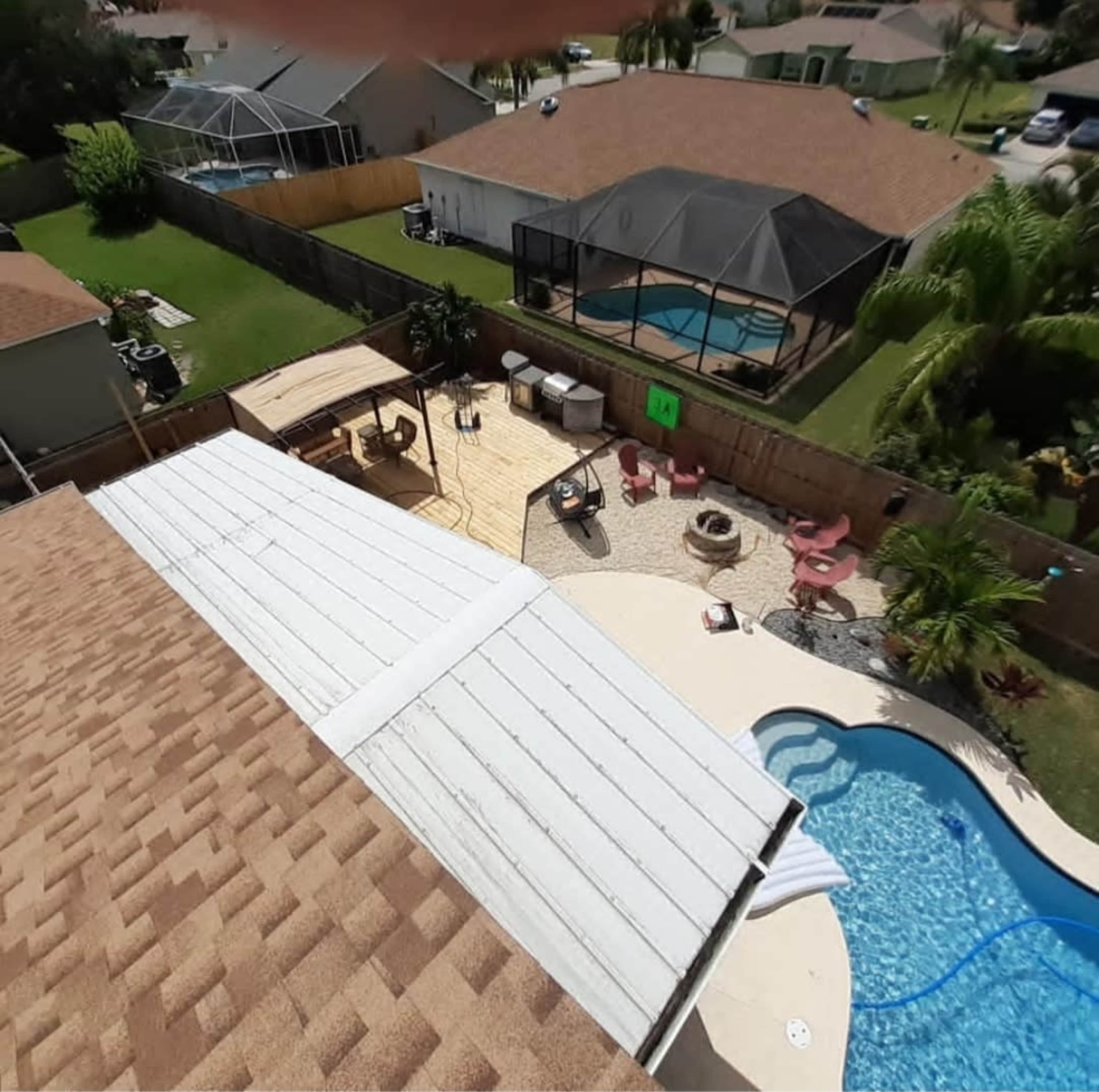 The image shows a backyard with a pool, wooden deck, and seating areas surrounded by houses and greenery.