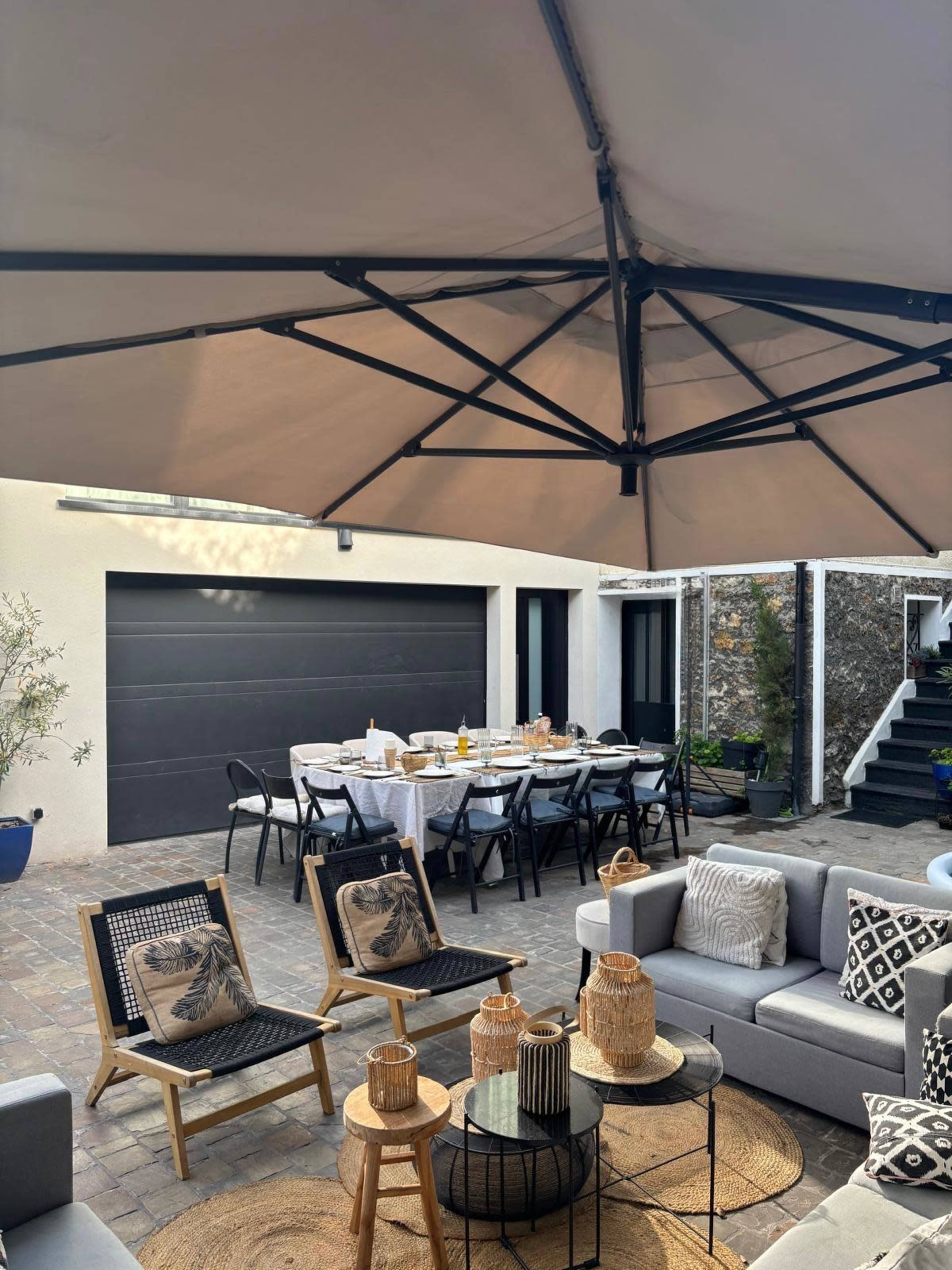 A patio area features a dining table set for a meal, surrounded by seating and sheltered under a large umbrella.