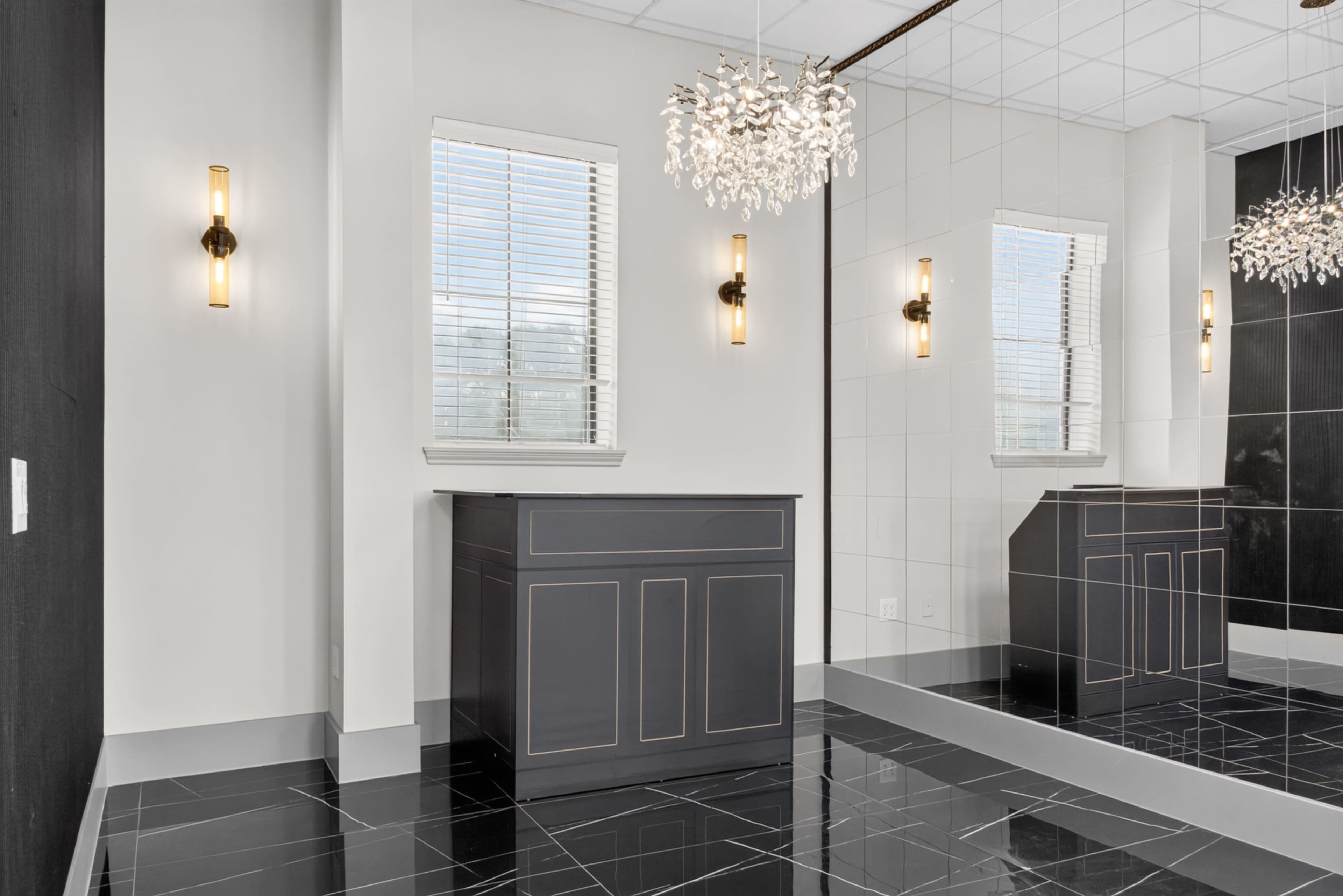 The interior features a sleek black and white design with a mirrored wall, a chandelier, and a vanity unit underneath the windows.