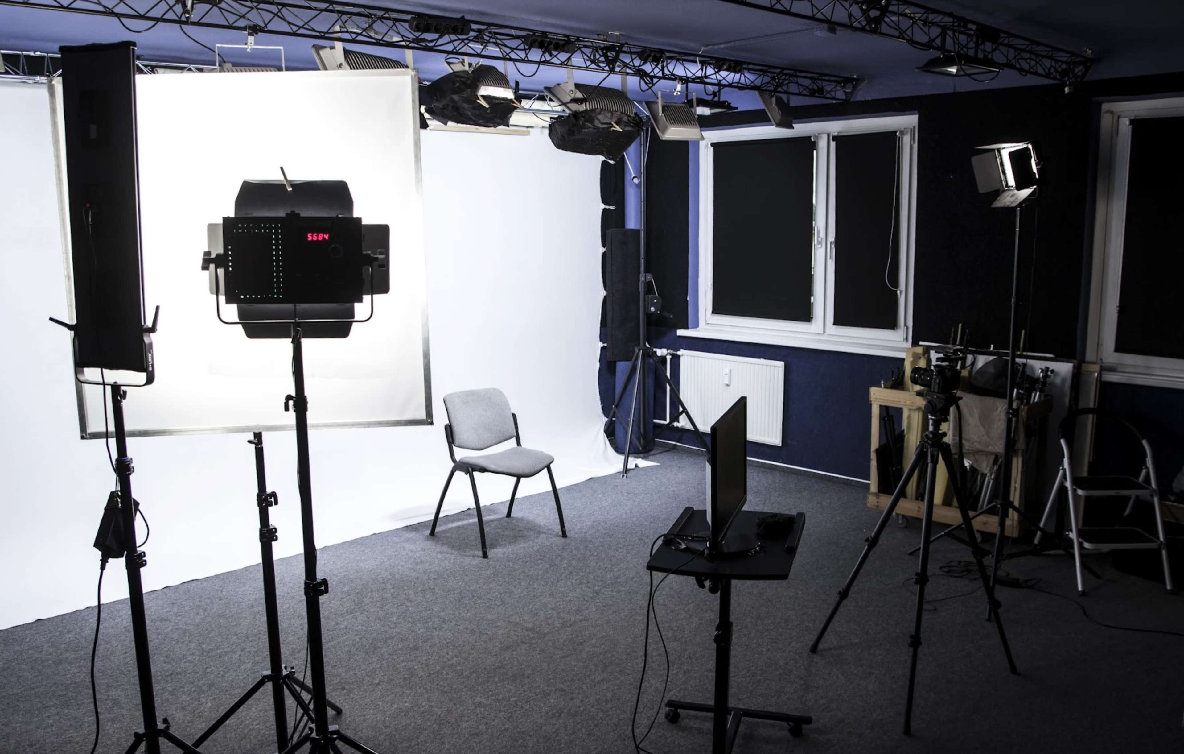 A well-equipped studio space features a backdrop, lighting equipment, a chair, and various cameras set up for recording.