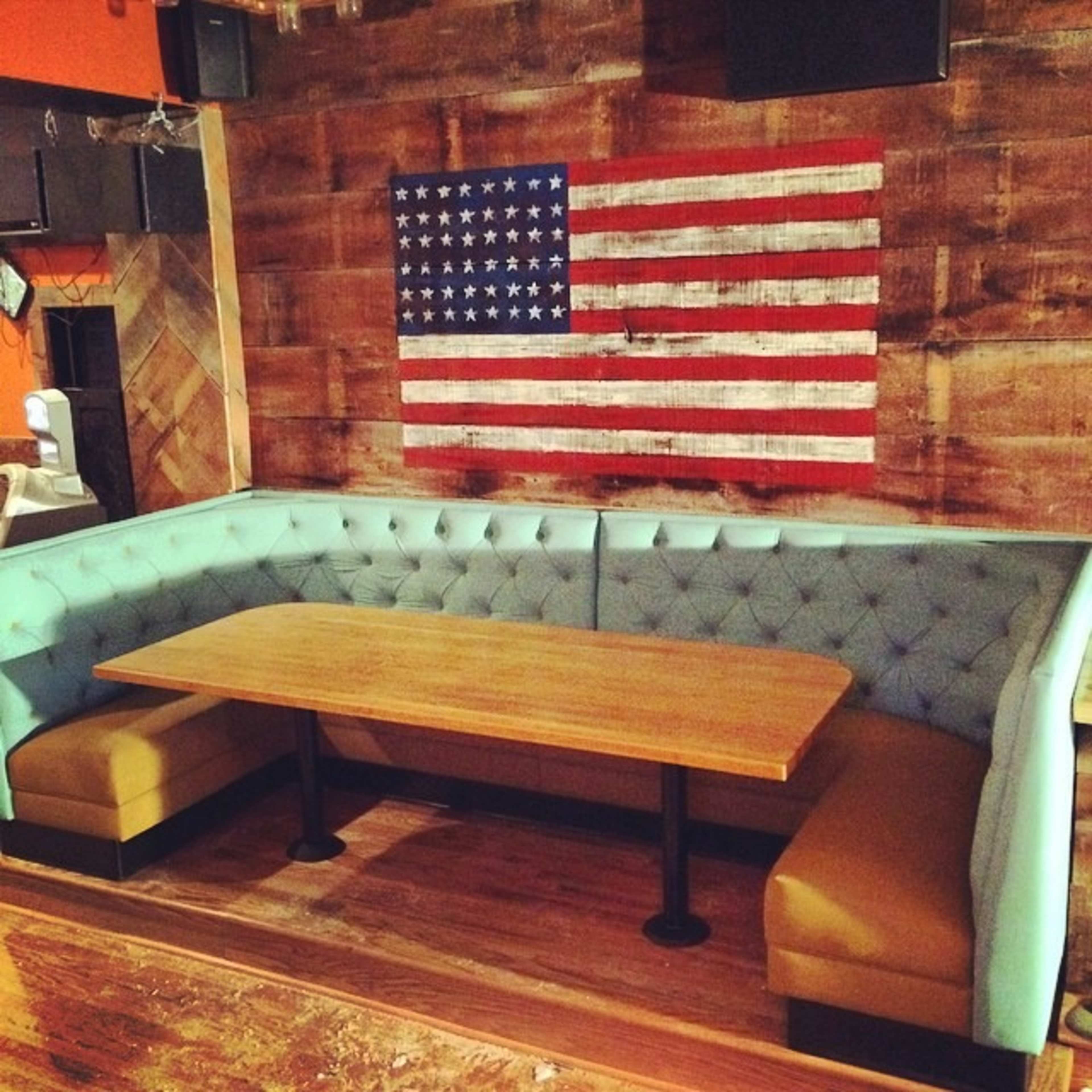 The image shows a corner seating booth with a wooden table and an American flag displayed on the wall behind it.