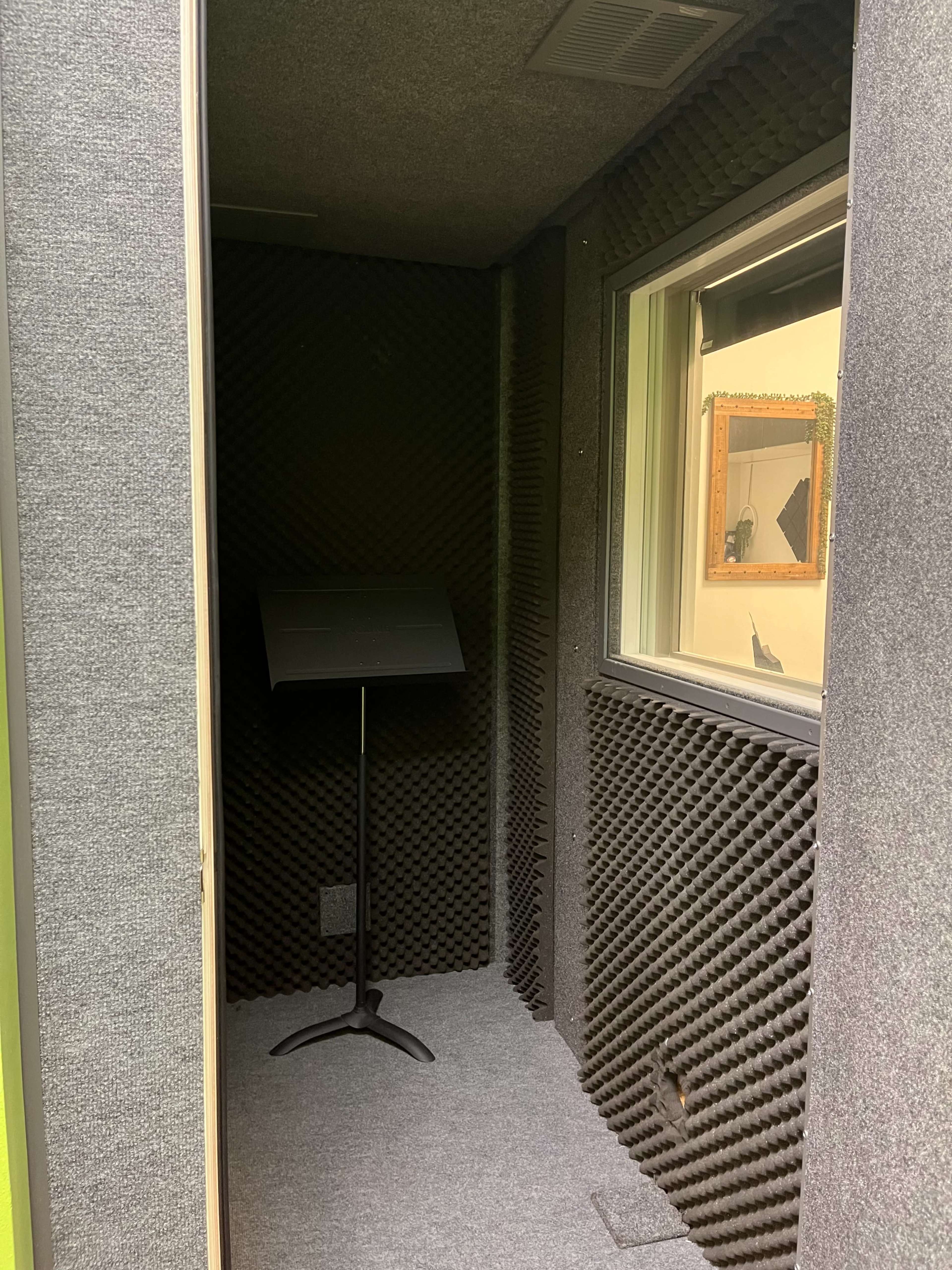 A soundproof booth features grey acoustic panels and a stand for holding music sheets.
