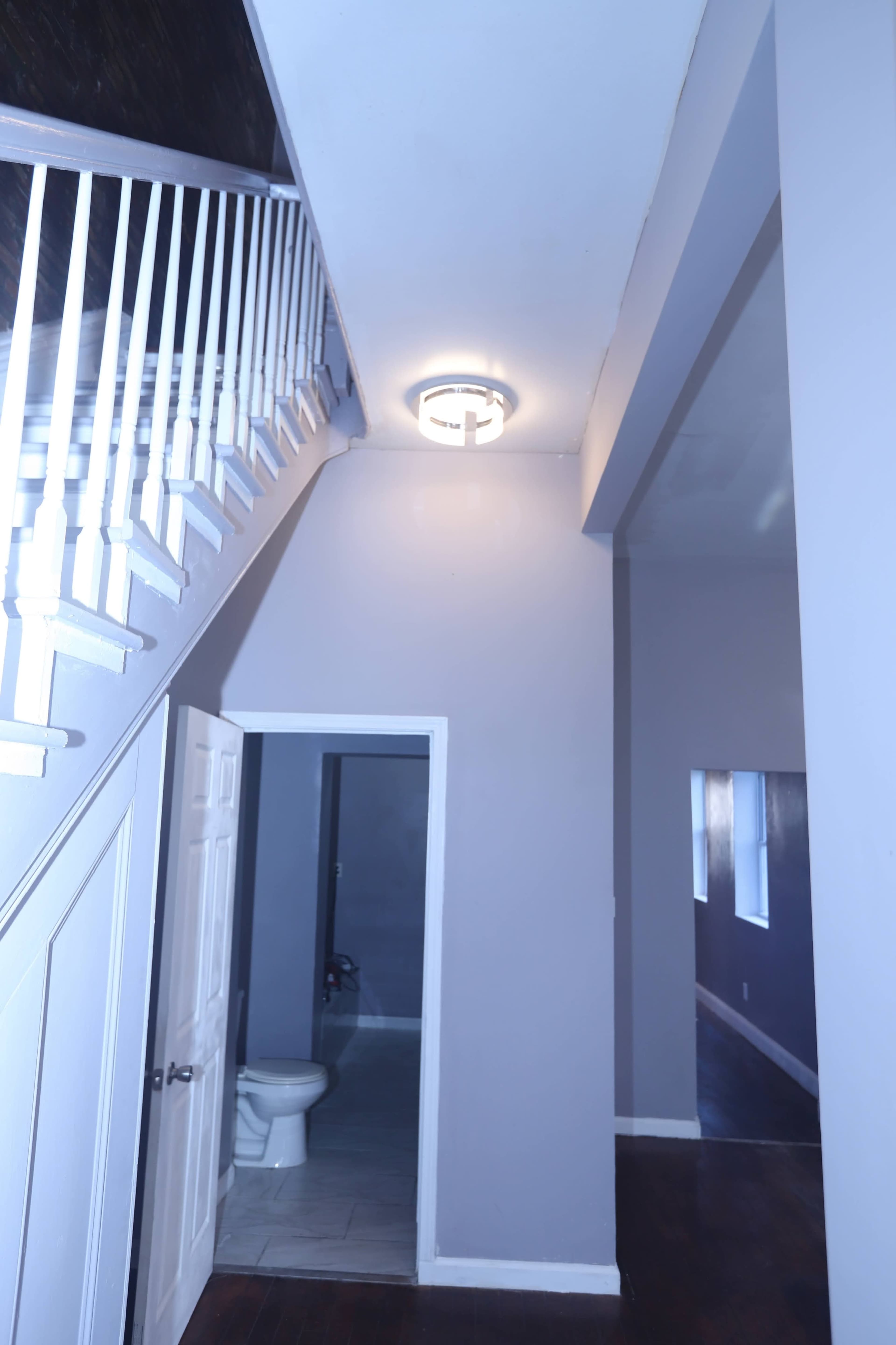The image shows a staircase leading to an upper level, with a door on the left and a light fixture on the ceiling in a hallway painted in light colors.