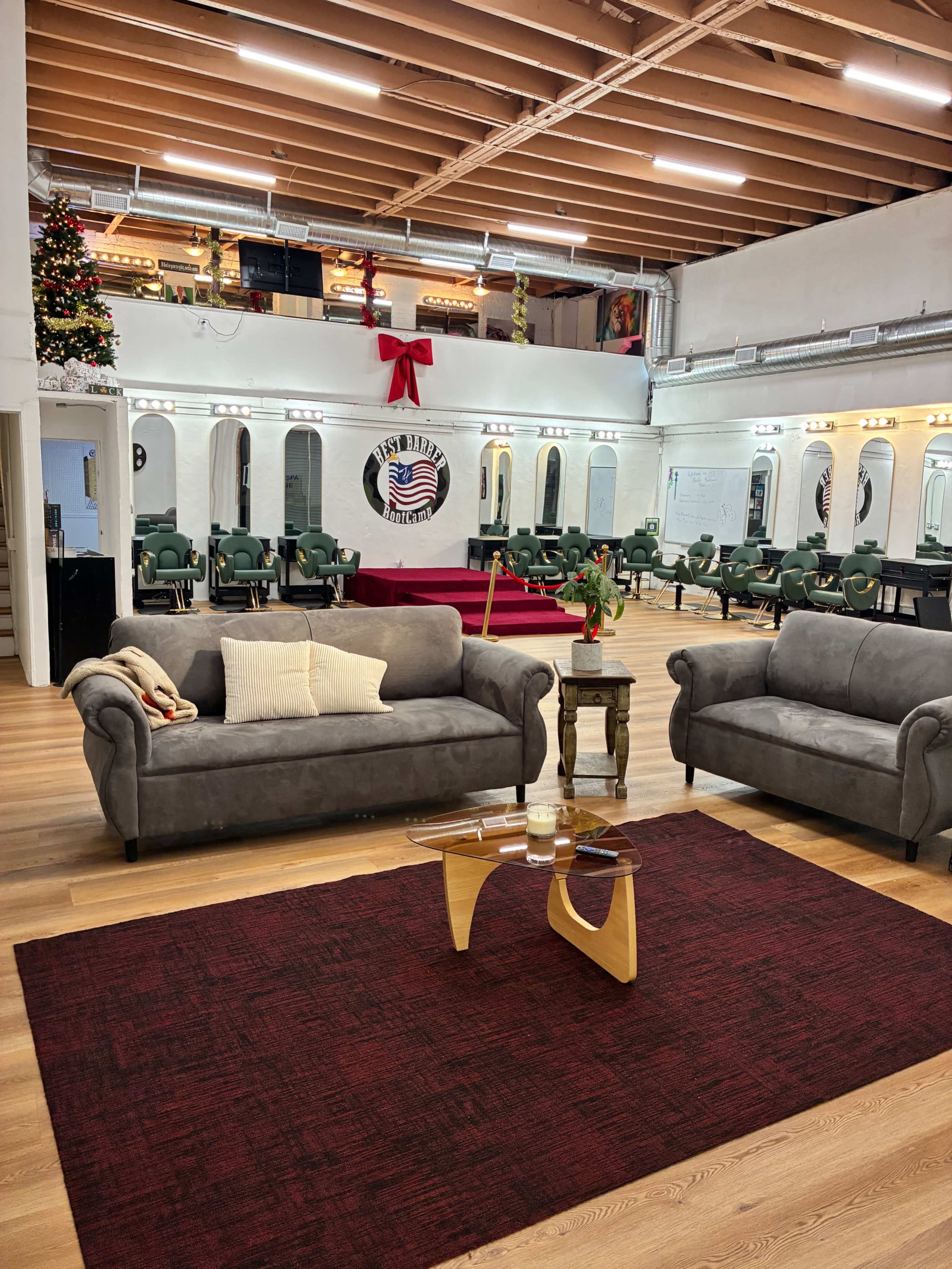 A modern salon interior features two gray sofas on a red rug facing a grooming station with multiple chairs and mirrors in a bright, spacious setting.